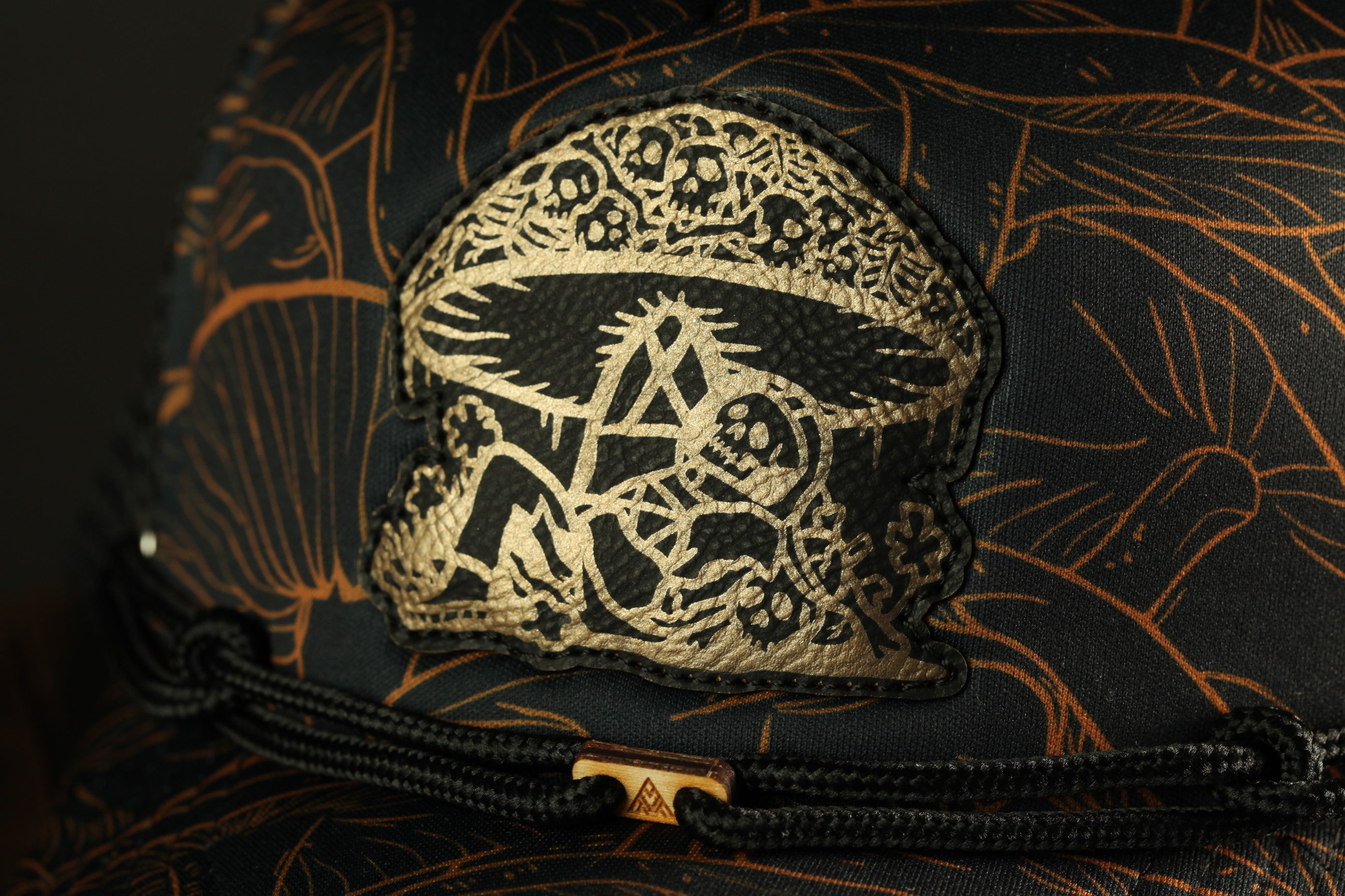 a close-up view of a black and gold patterned fabric, possibly a hat or bag, with a distinctive emblem or design on the front.