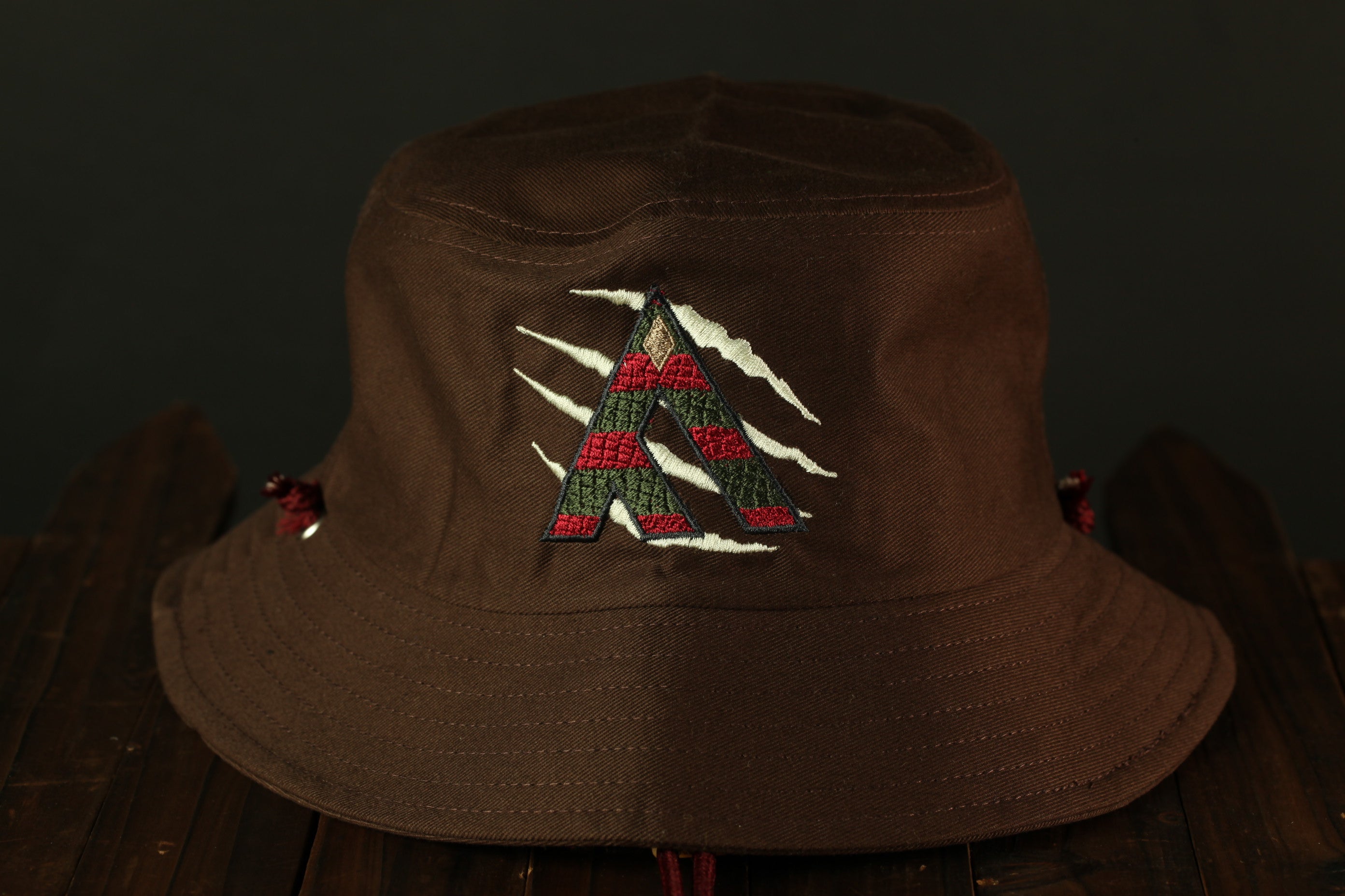 A brown bucket hat with a red and green embroidered design on the front.