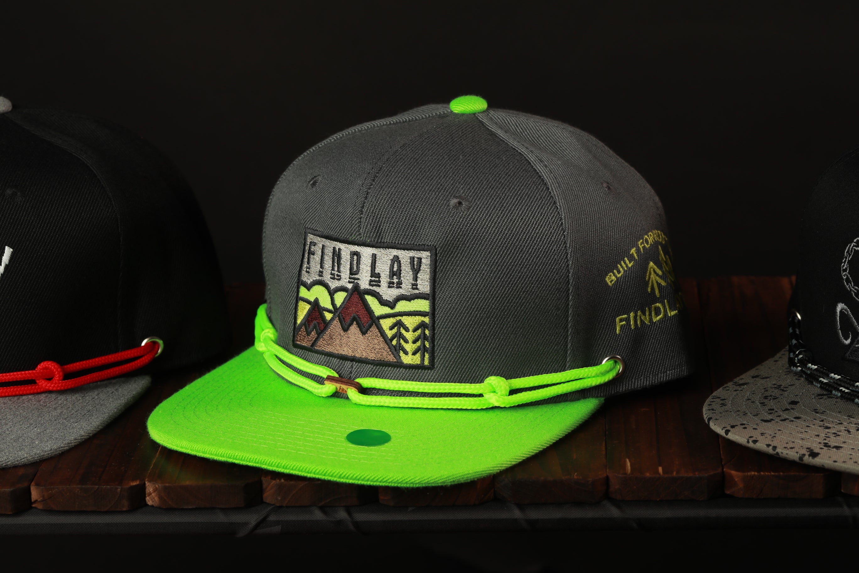 A gray baseball cap with a green brim and a graphic design on the front, sitting on a wooden surface.
