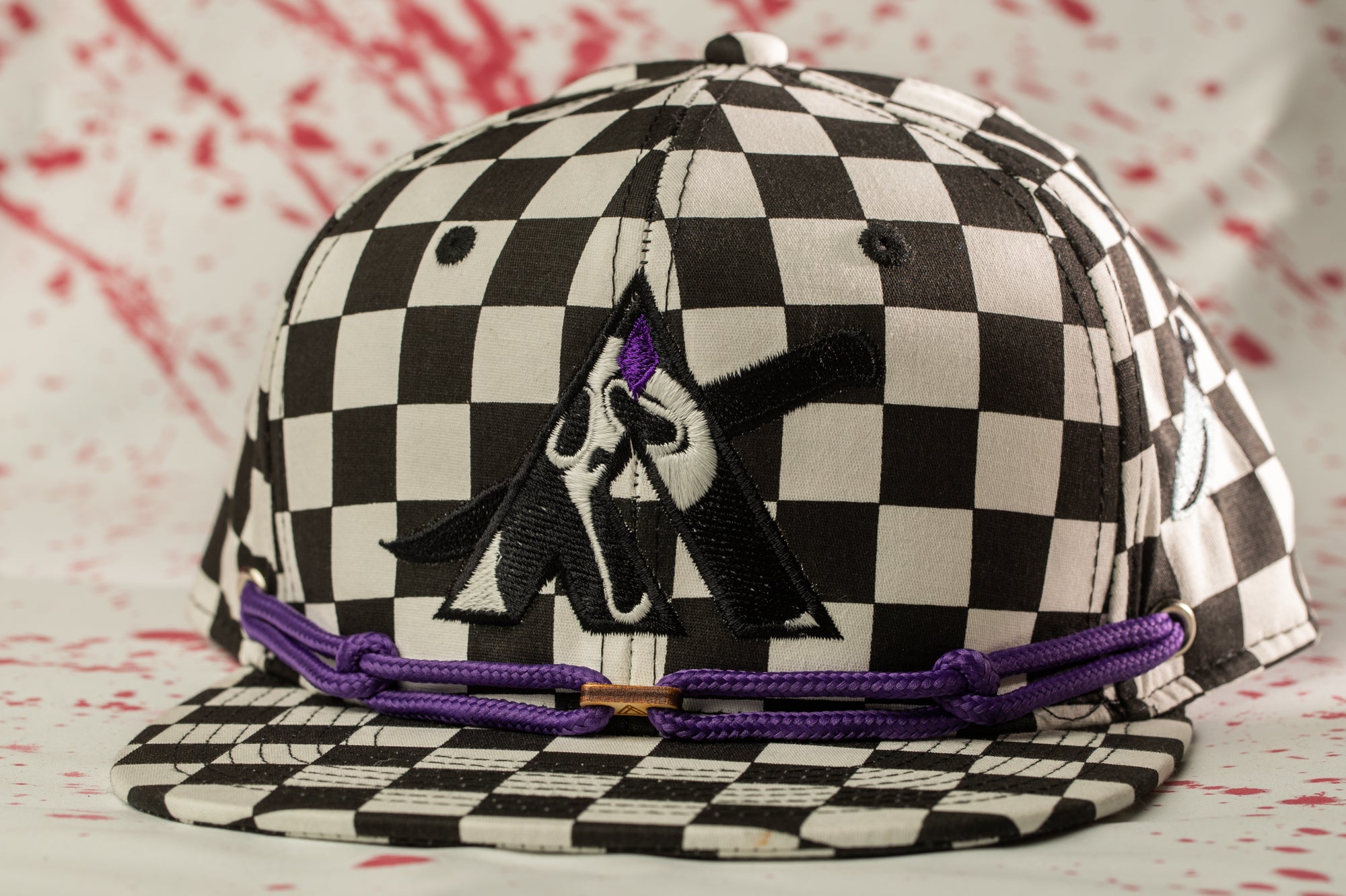 A black and white checkered baseball cap with a purple string and a graphic design on the front.