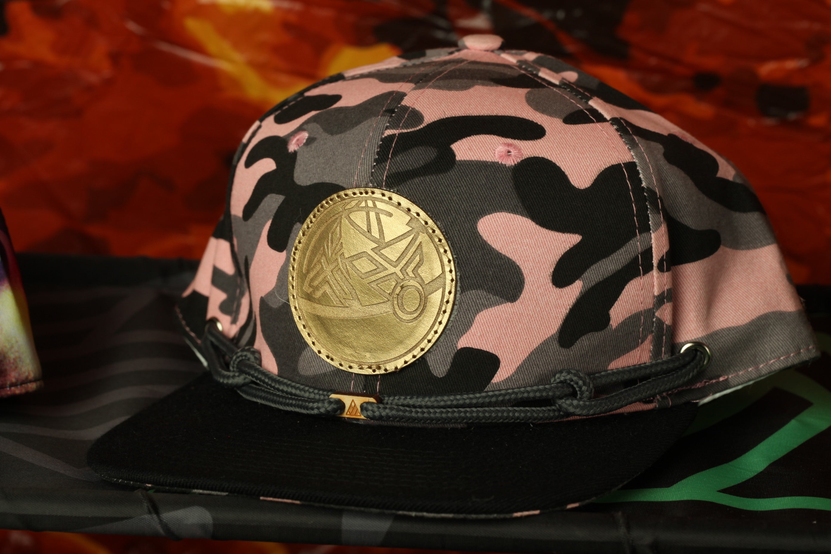 A pink and black camouflage baseball cap with a gold emblem on the front.