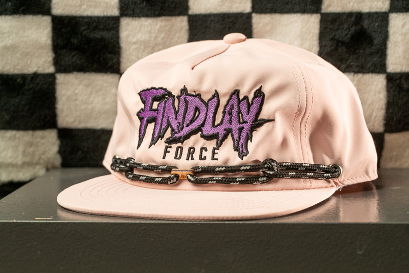 A pink baseball cap with the text "FINDlay Force" printed on it, sitting on a black surface against a checkered background.