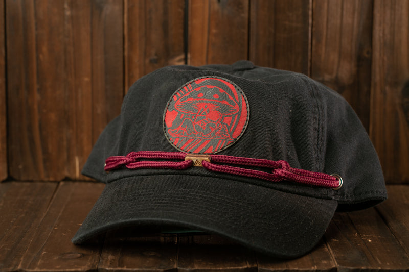 A black baseball cap with a red mushroom design on the front, resting on a wooden surface.