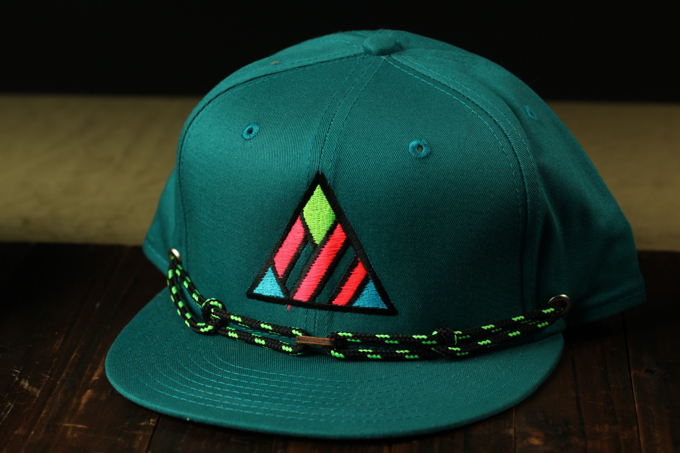 A green baseball cap with a colorful geometric pattern on the front, featuring a black and green braided strap.