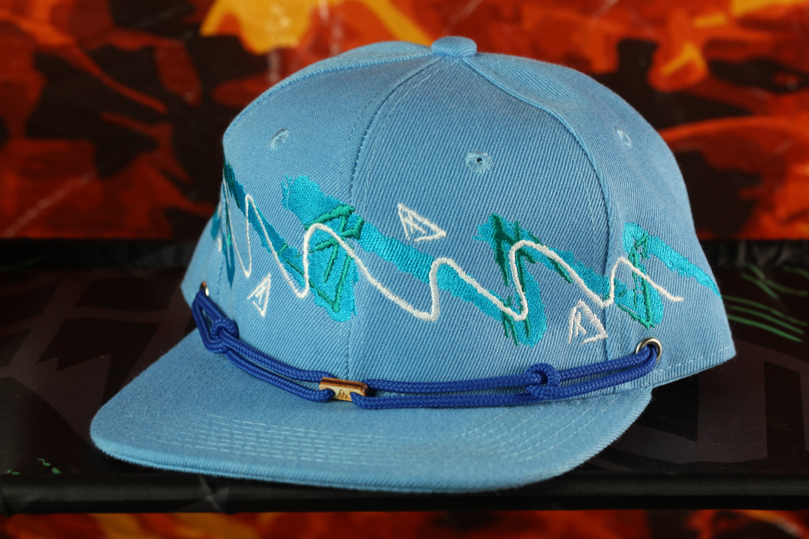 A blue baseball cap with a decorative pattern on the front, sitting on a surface against a colorful background.