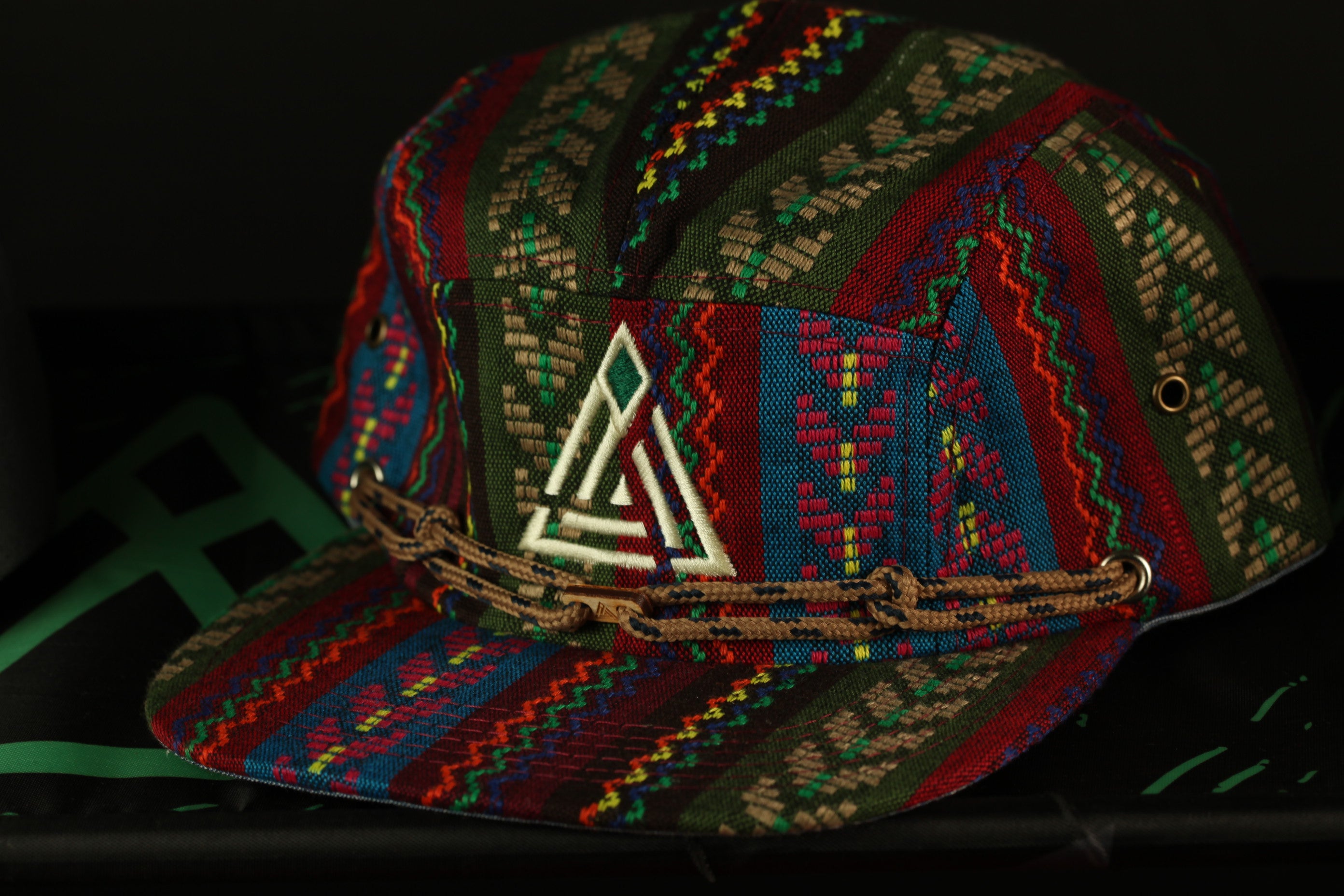 A colorful, patterned baseball cap with a geometric design and a chain strap.