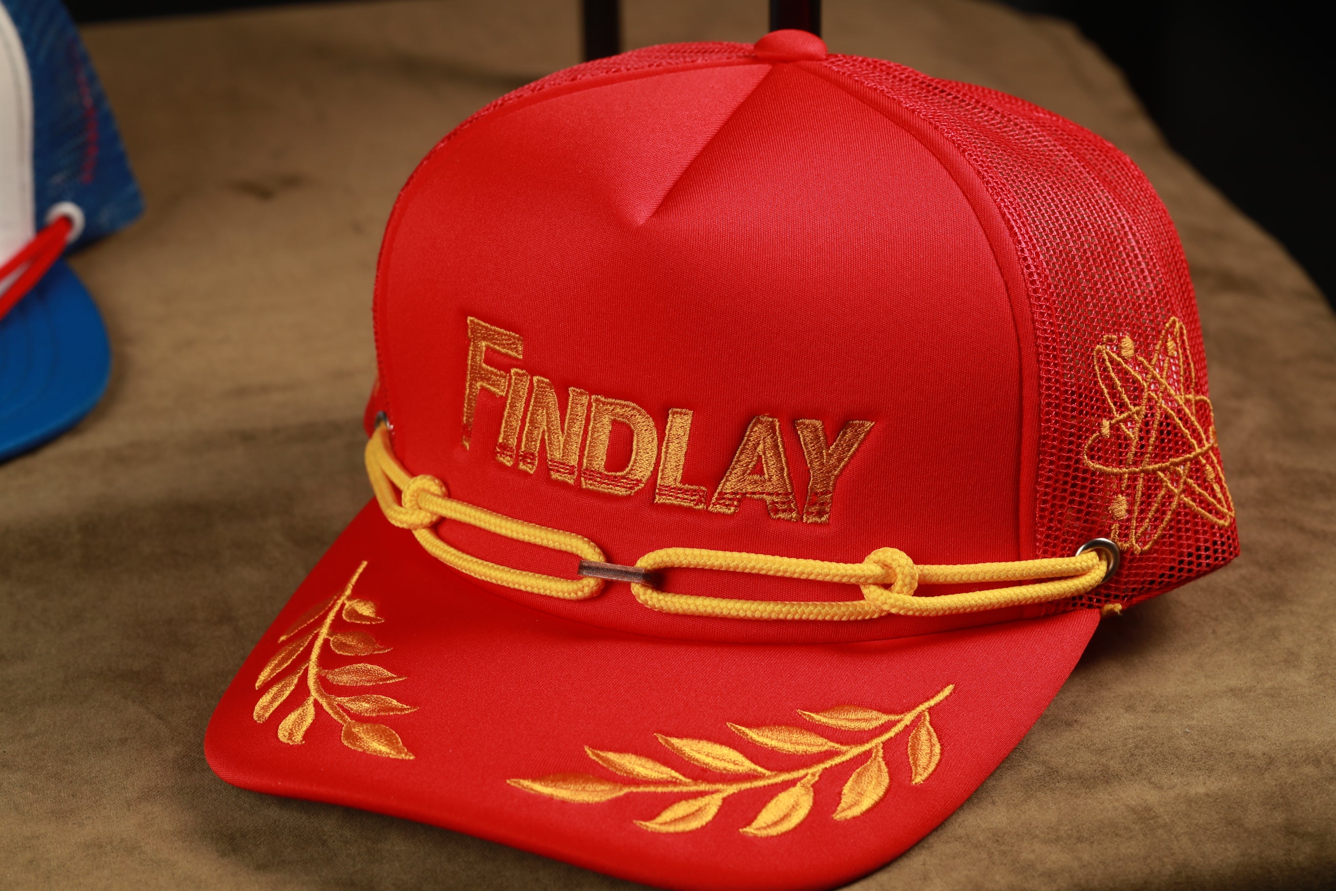 A red baseball cap with the word "Findlay" embroidered on it, sitting on a brown surface.