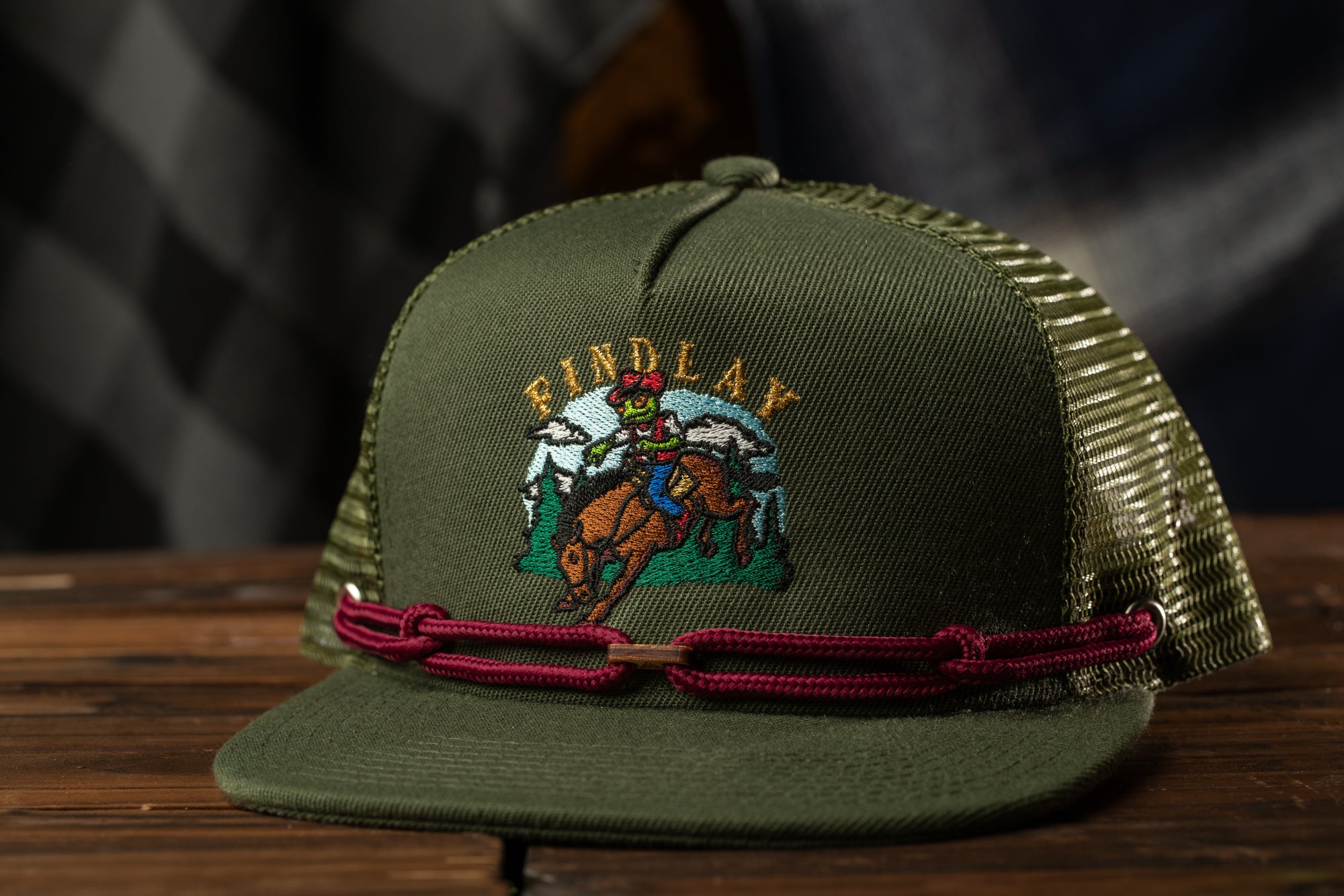 A green baseball cap with a graphic of a cowboy riding a bucking bronco, along with the text "FINDlay" on the front.