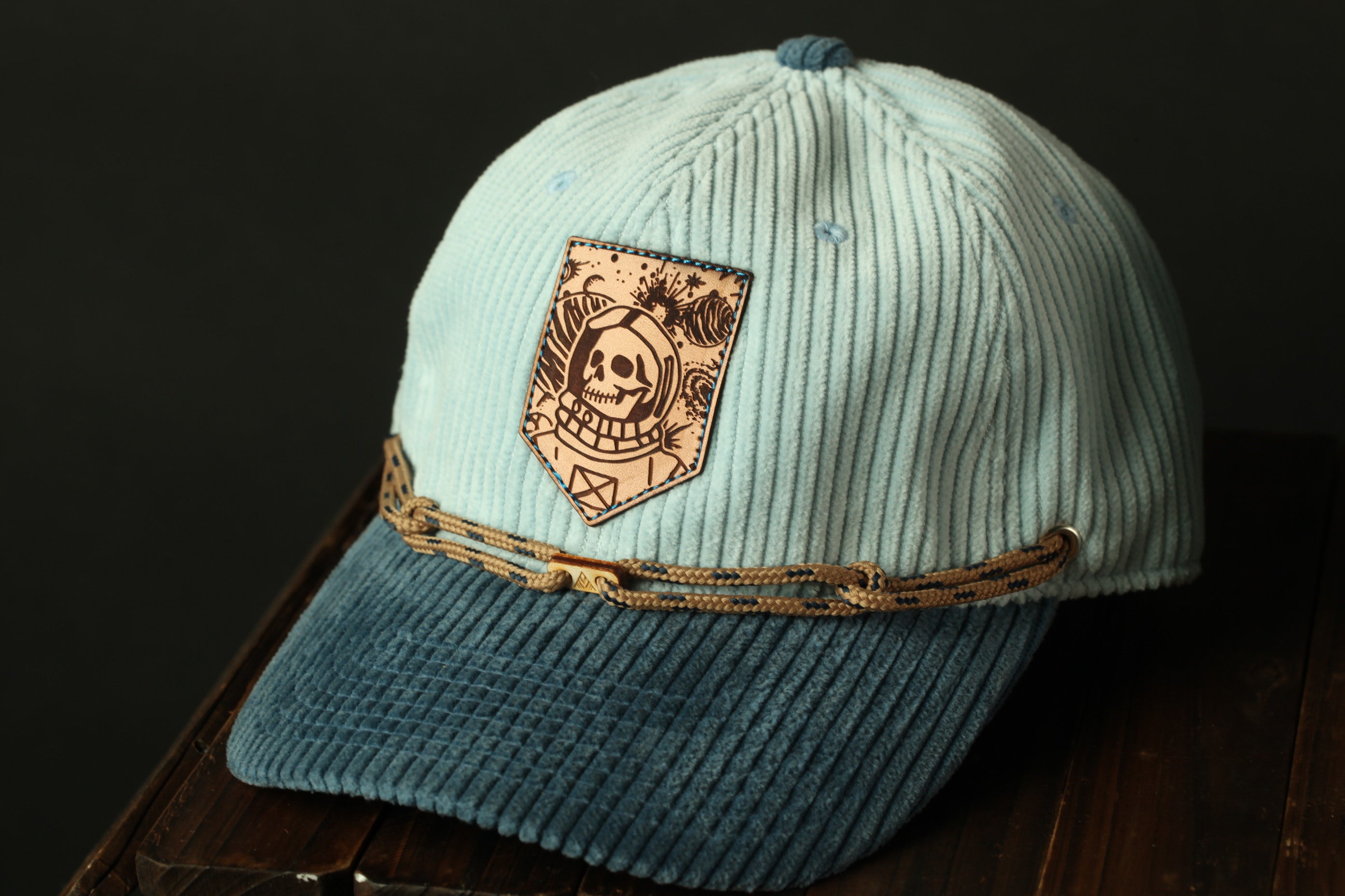 A light blue baseball cap with a skull and crossbones patch on the front, sitting on a wooden surface.