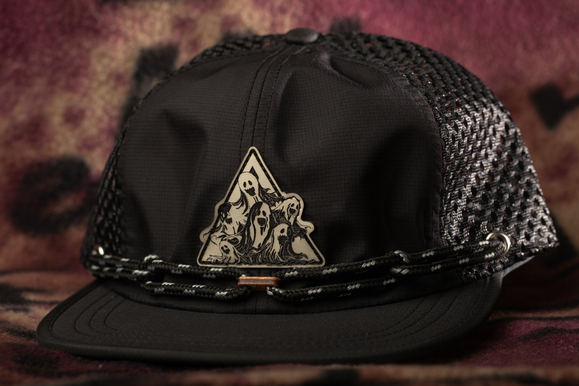 A black baseball cap with a mesh back and a triangular emblem featuring a group of people.