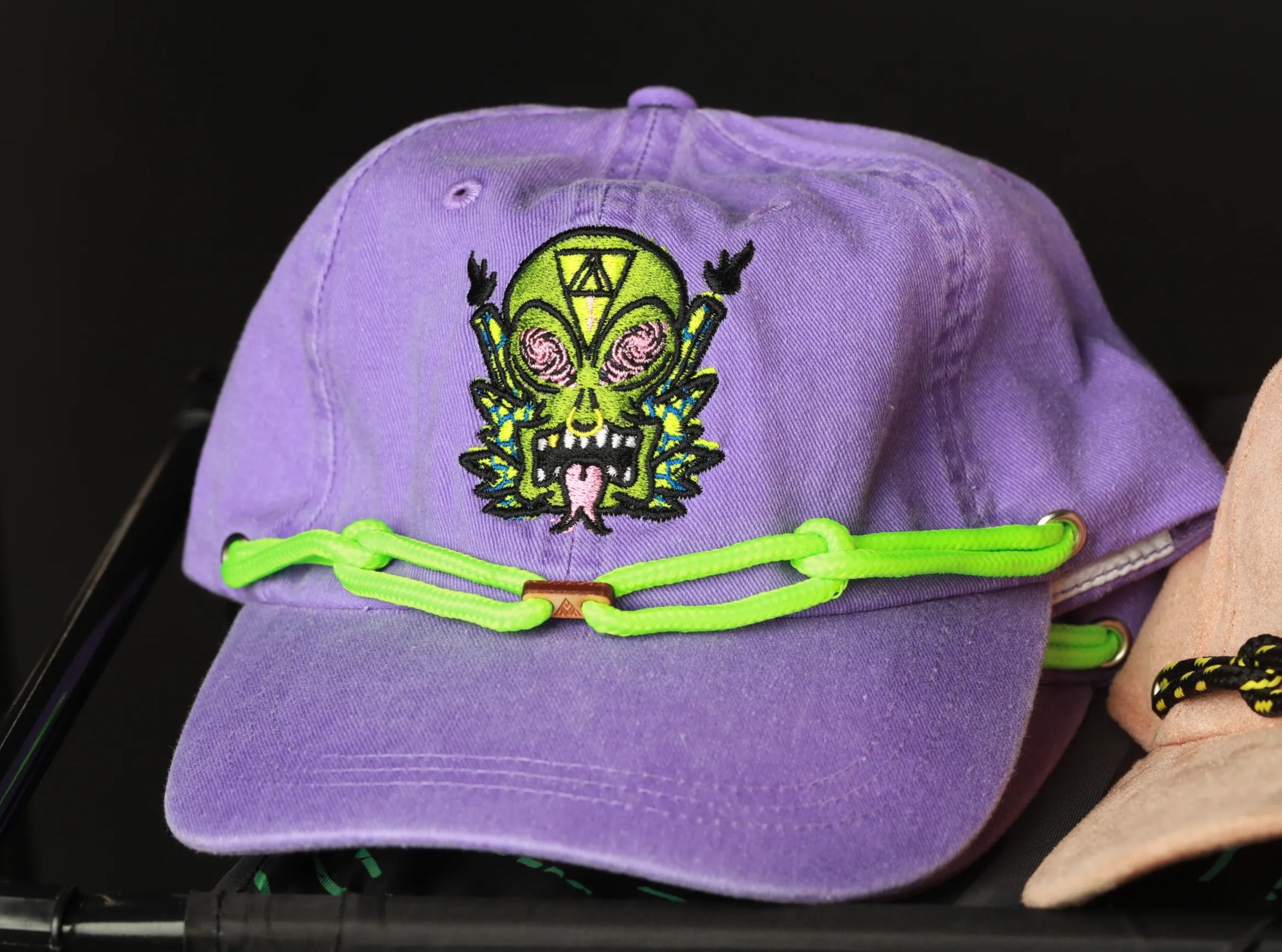 A purple baseball cap with a green and yellow skull design and a neon green chain strap.