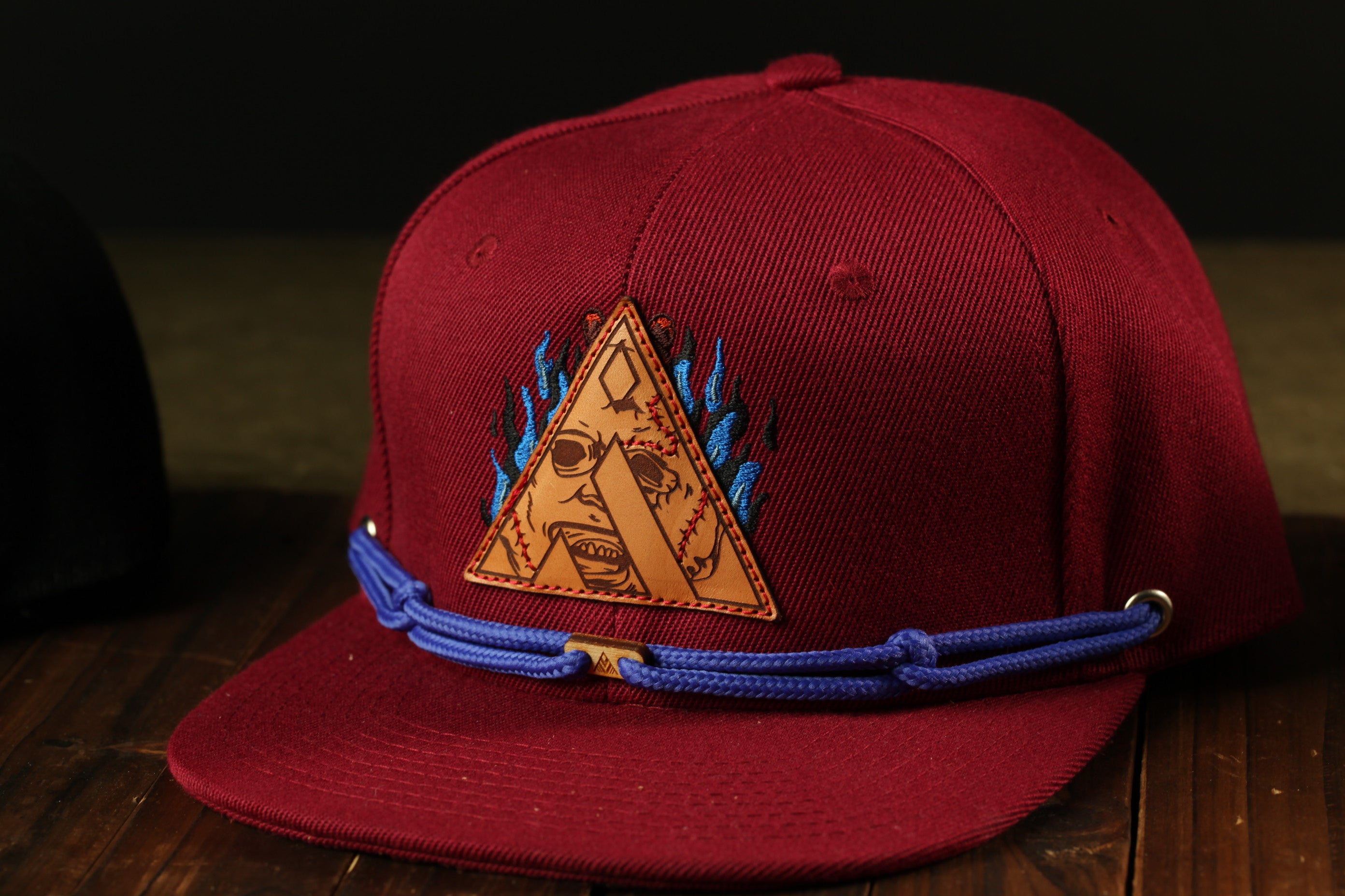 A red baseball cap with a triangular logo and blue straps is displayed on a wooden surface.