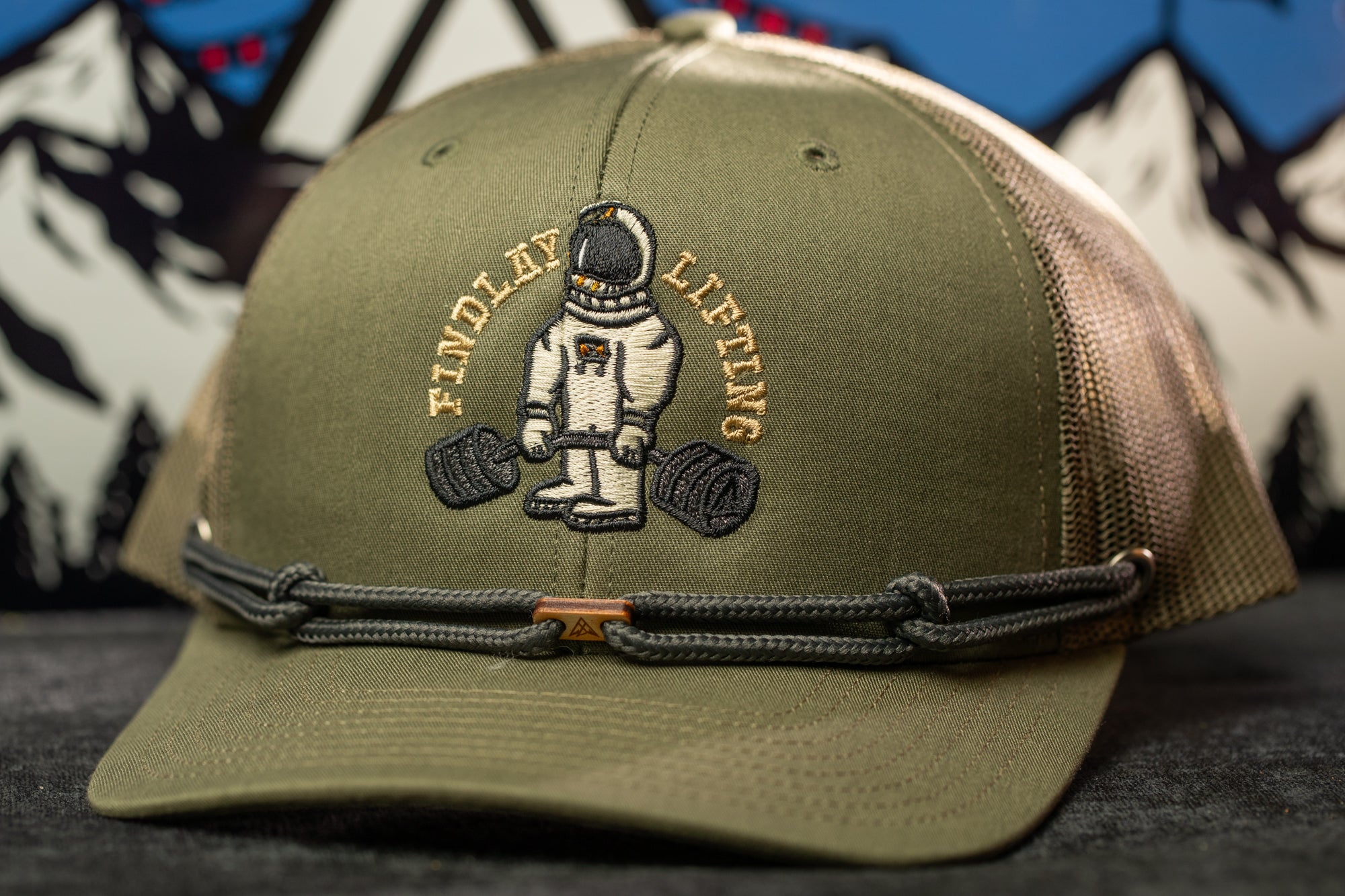 A green baseball cap with an embroidered design of an astronaut lifting weights.