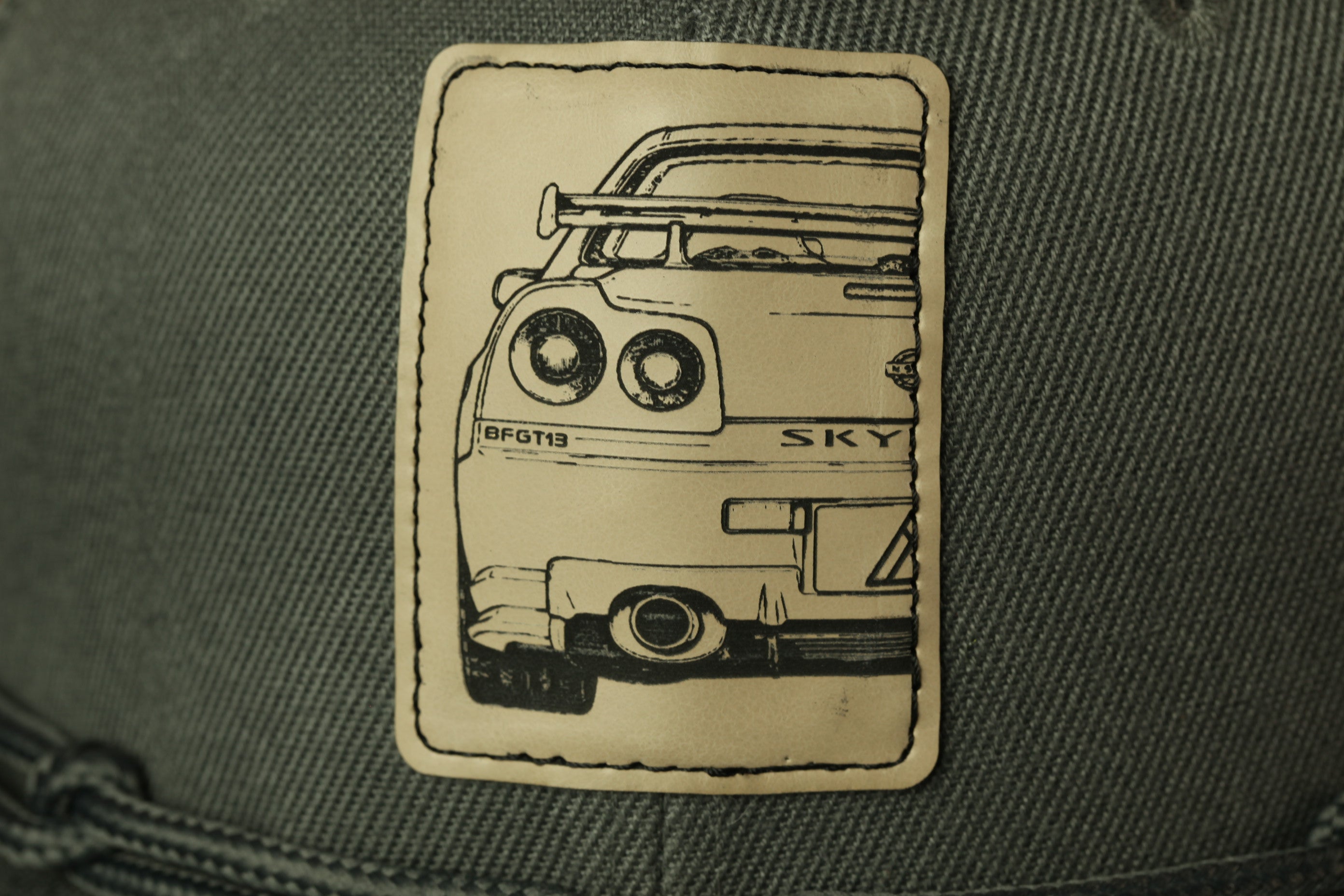 A close-up of a beige patch with a black and white illustration of a car on it, attached to a gray fabric surface.