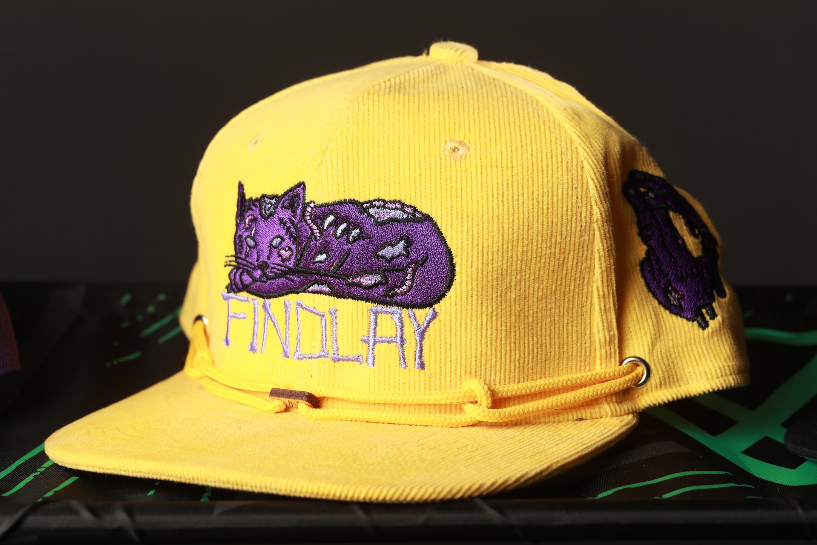 A yellow baseball cap with a purple cat embroidered on it.