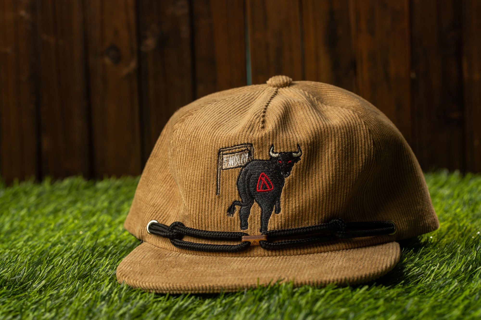 A brown baseball cap with a black bull embroidered on it, placed on a grassy surface.