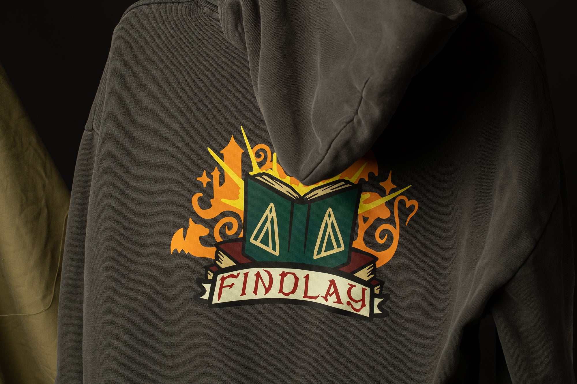a gray hoodie with a colorful graphic design on the back. The design features a book with a triangle symbol on the cover, surrounded by orange and yellow elements. The word "FINDLAY" is written below the book.