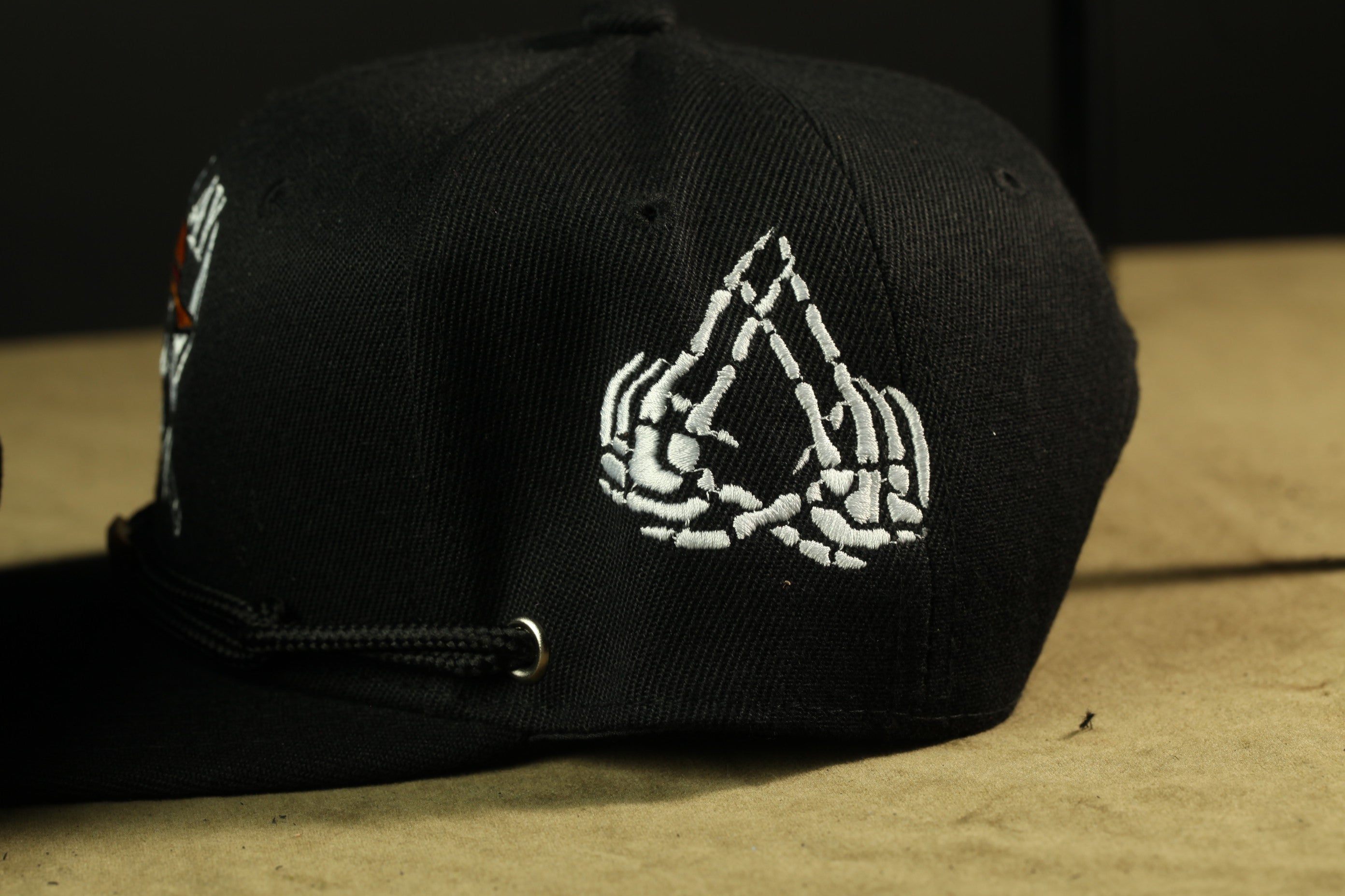 A black baseball cap with a white skeleton hand embroidered on the side.
