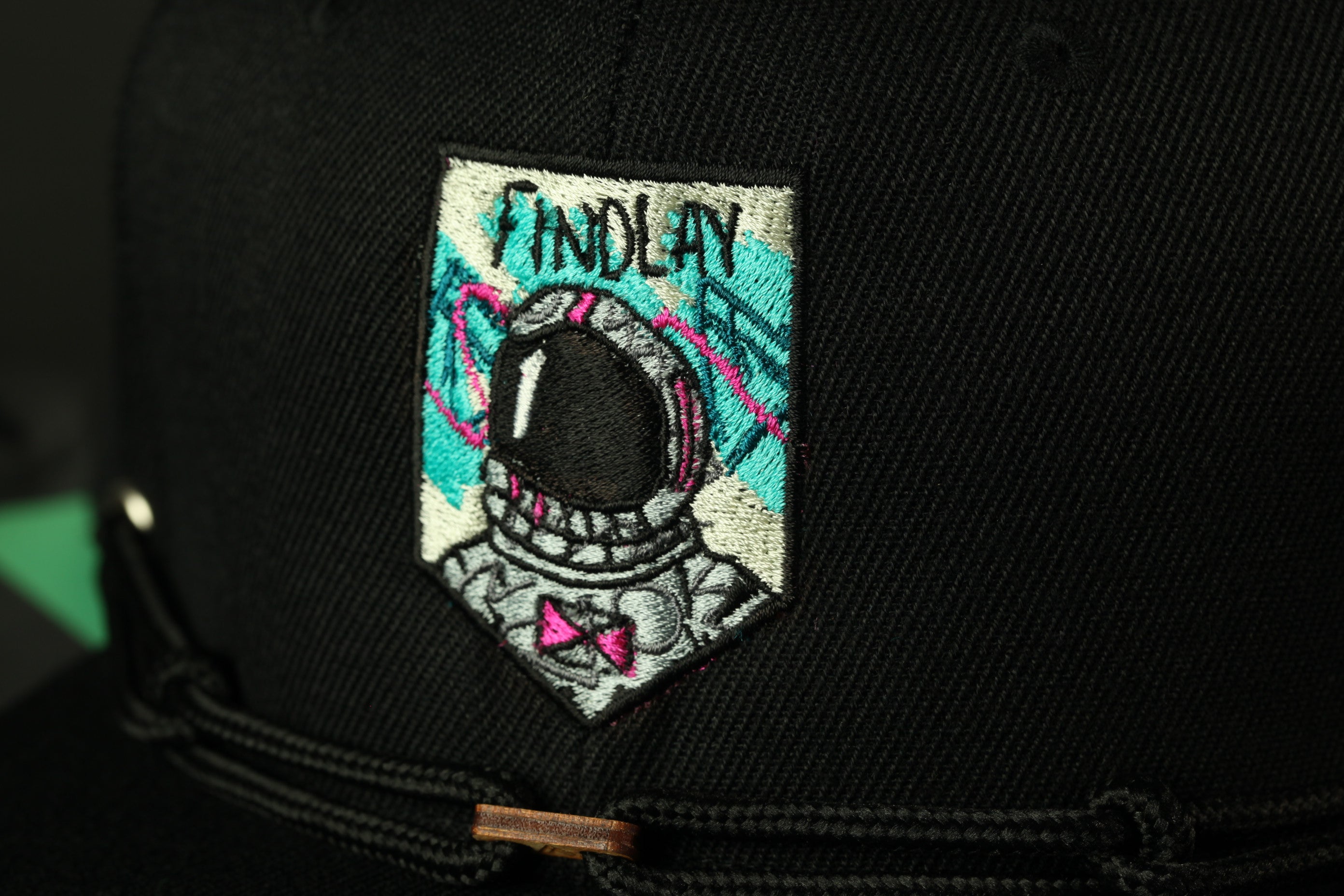 A close-up view of a black baseball cap with a colorful patch featuring an astronaut's helmet and the word "FINDlay" printed on it.