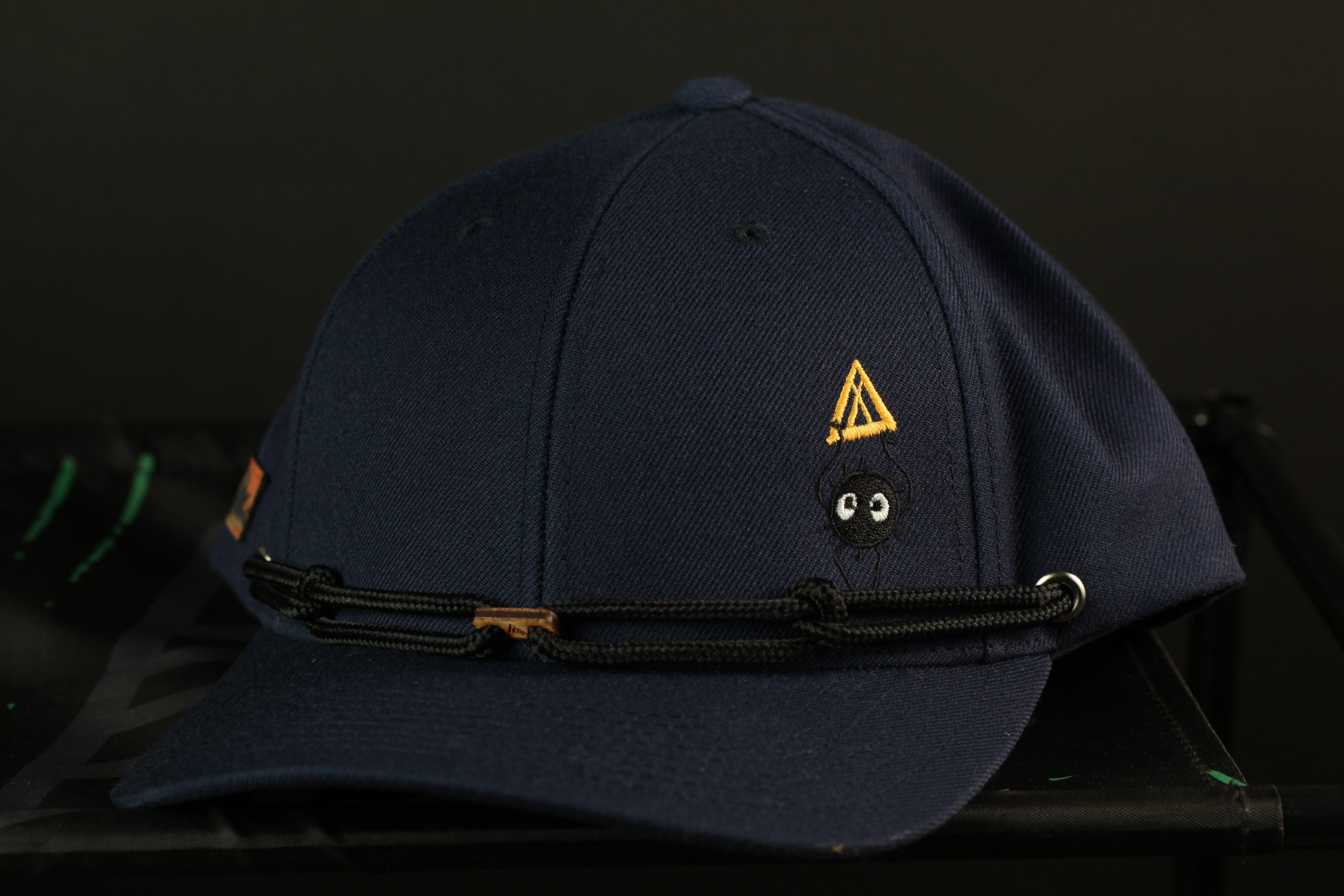 A navy blue baseball cap with a yellow triangle and a small black spider embroidered on the front.