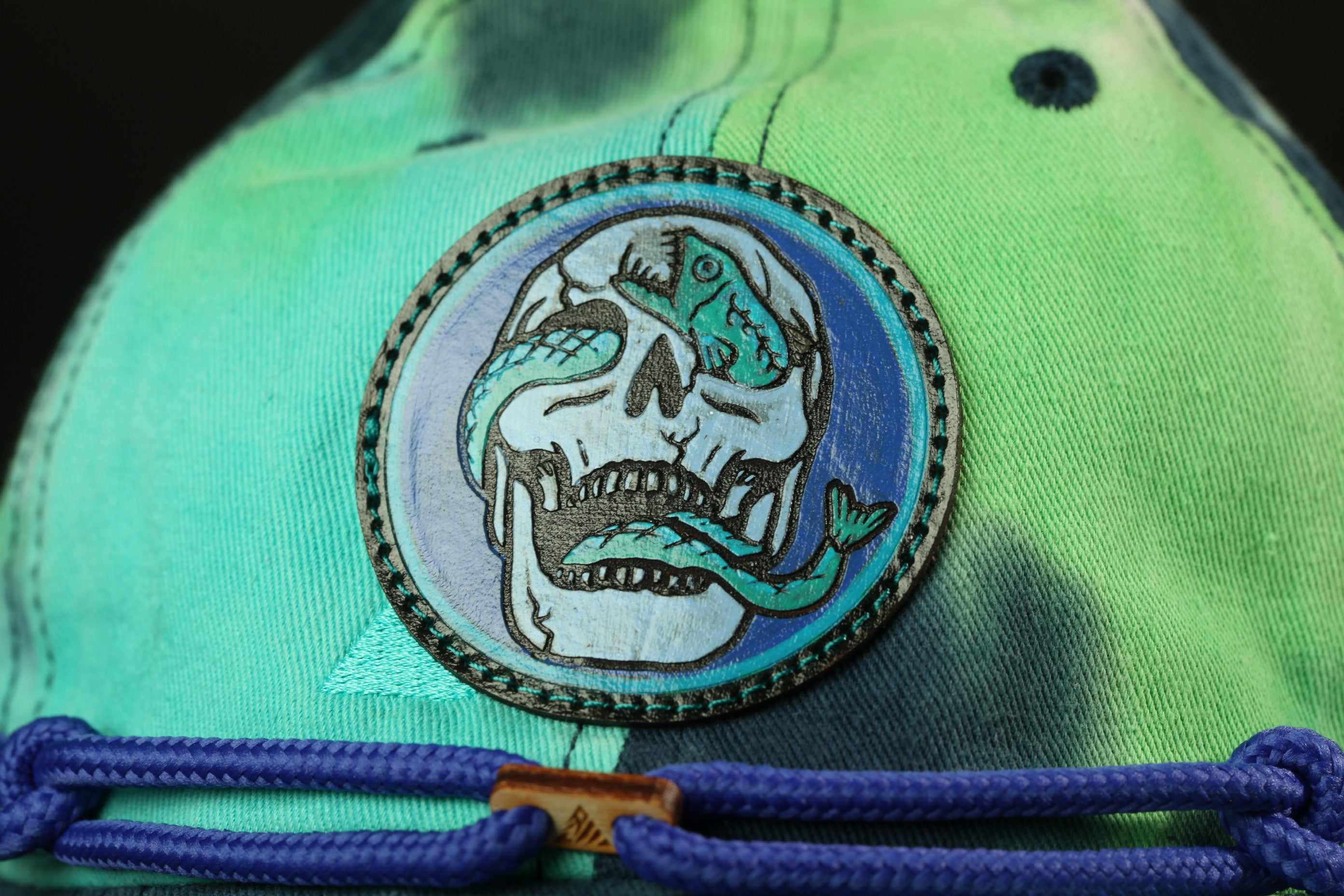 a close-up view of a tie-dye baseball cap with a skull and snake motif.