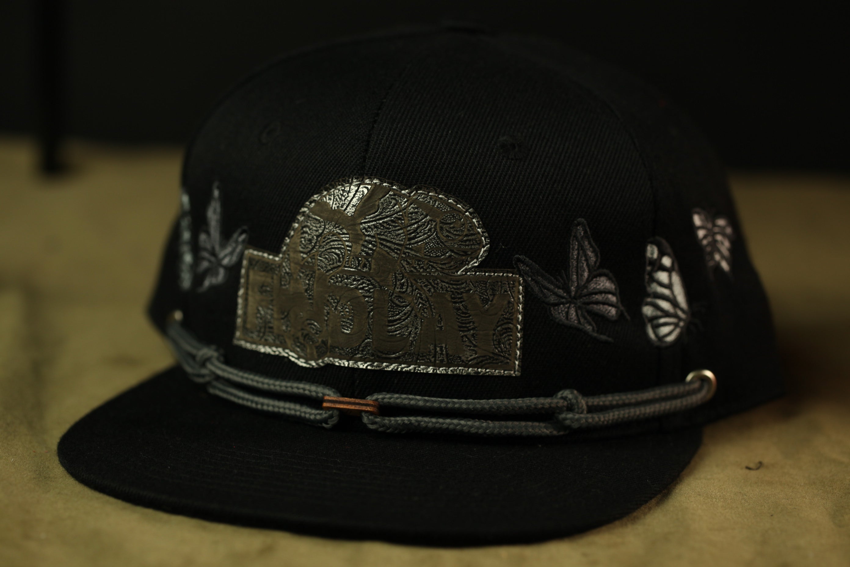 A black baseball cap with a decorative metal patch and a gray metal buckle.