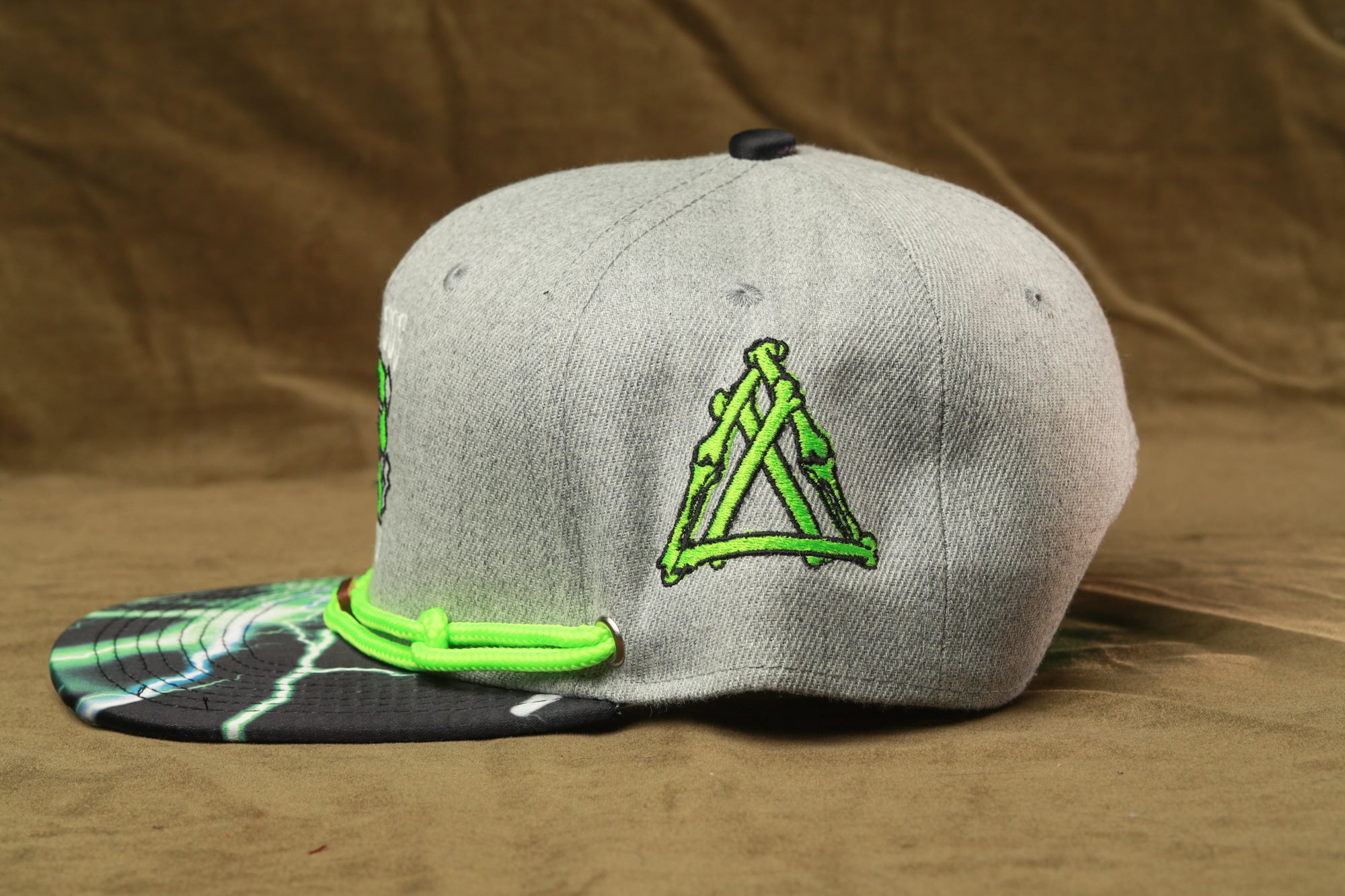 A gray baseball cap with a green triangle design on the front, sitting on a brown surface.
