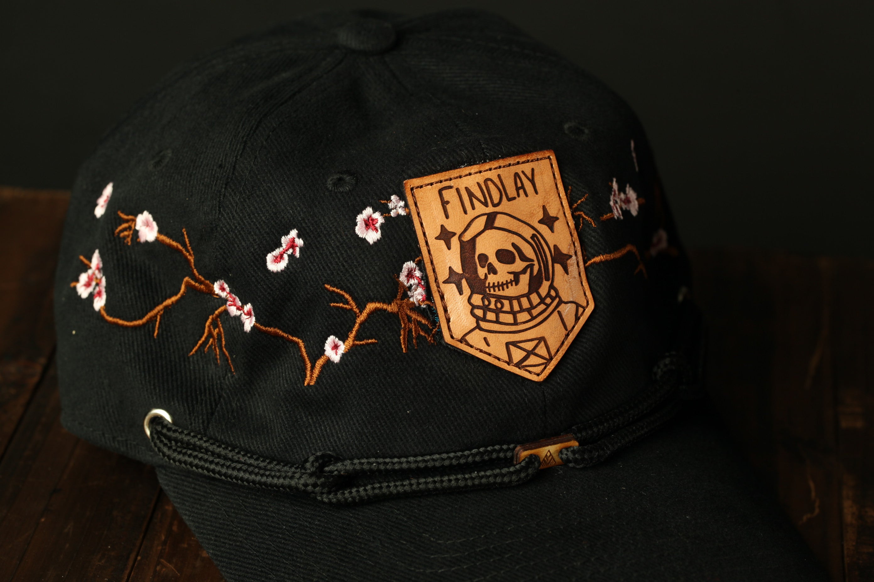 A black baseball cap with a floral design and a skull-like patch on the front.
