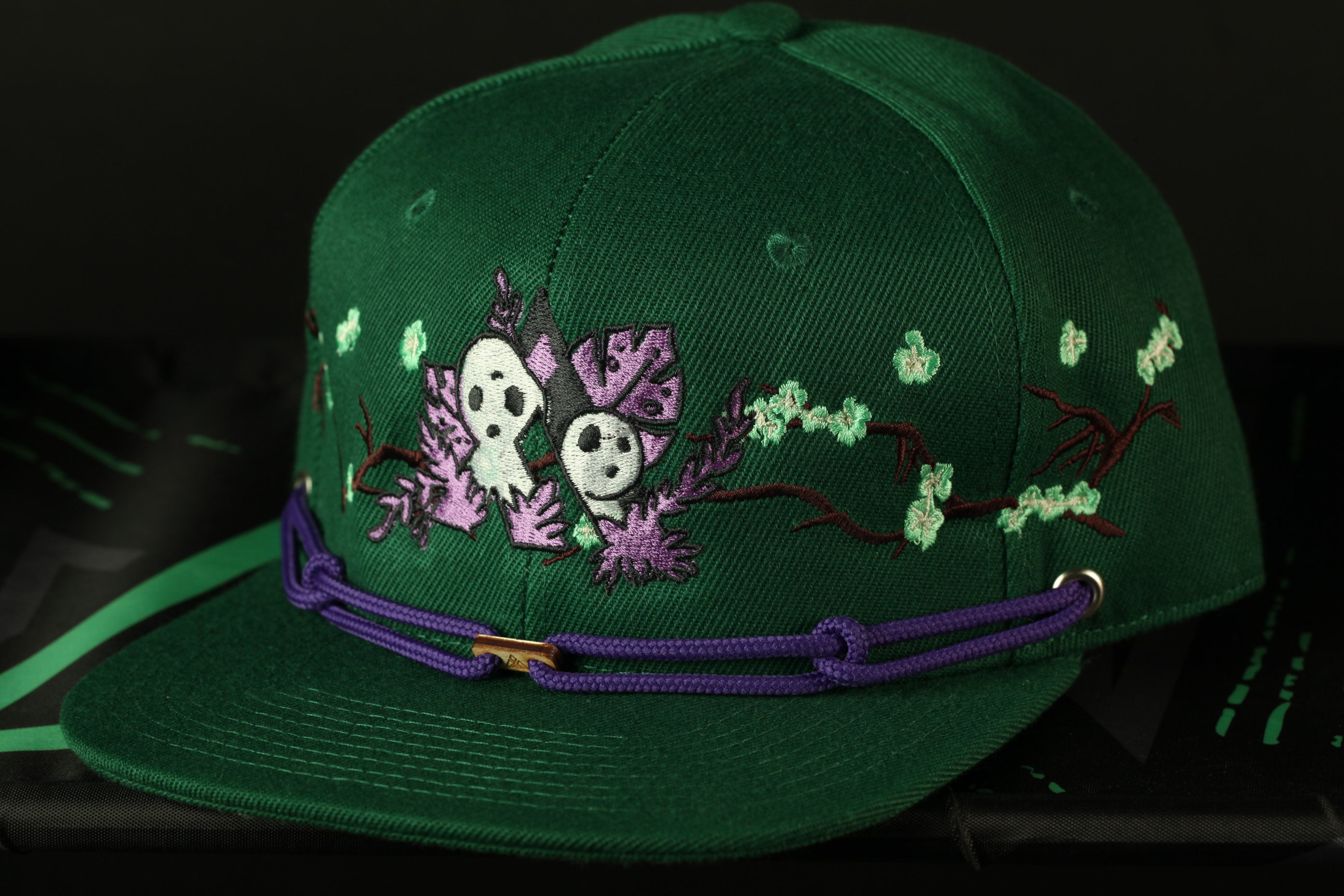 A green baseball cap with purple and white floral embroidery and a purple strap.