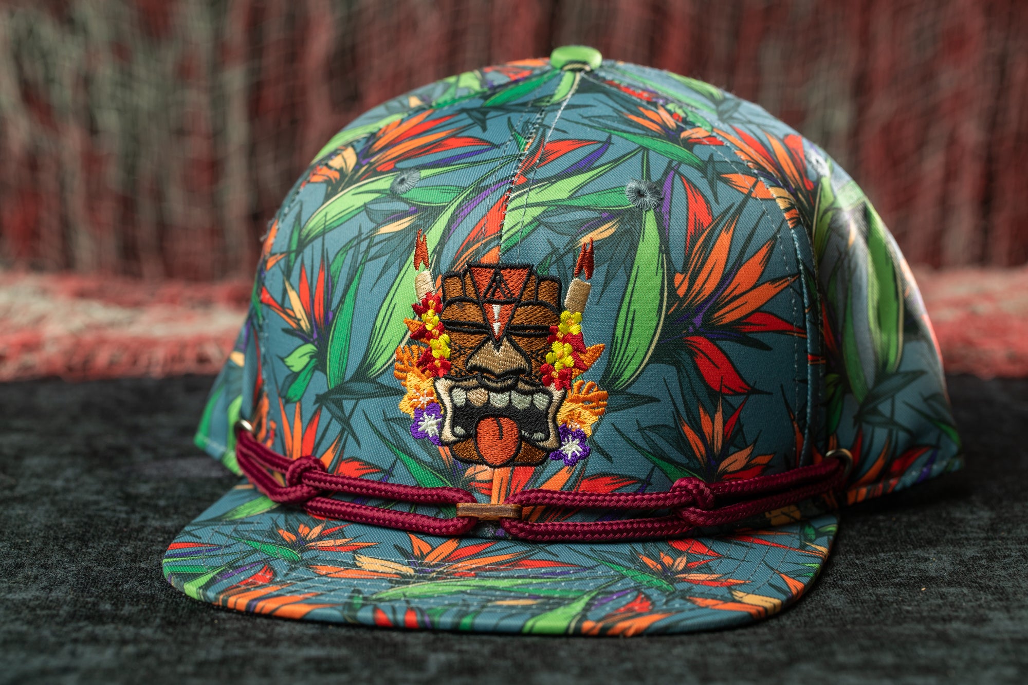 A colorful, patterned baseball cap with a tropical design and a tiki mask motif.