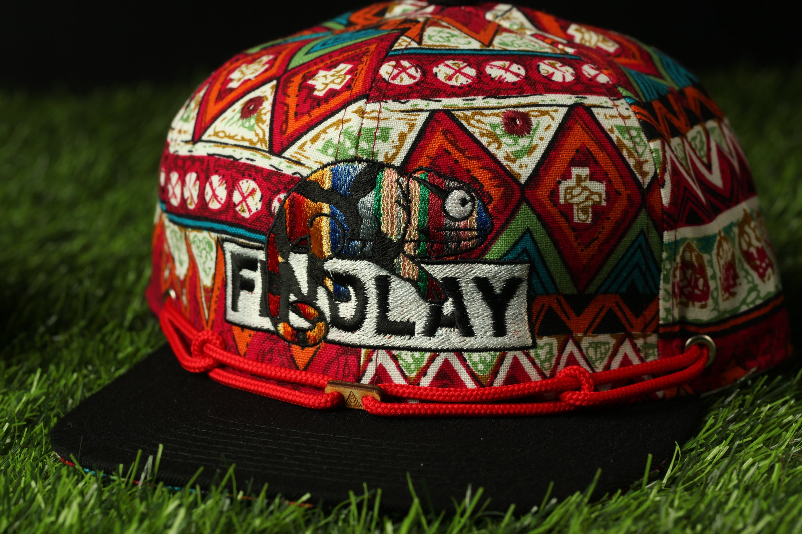 A colorful, patterned baseball cap with a red string and the word "FINDlay" embroidered on it, sitting on a grassy surface.