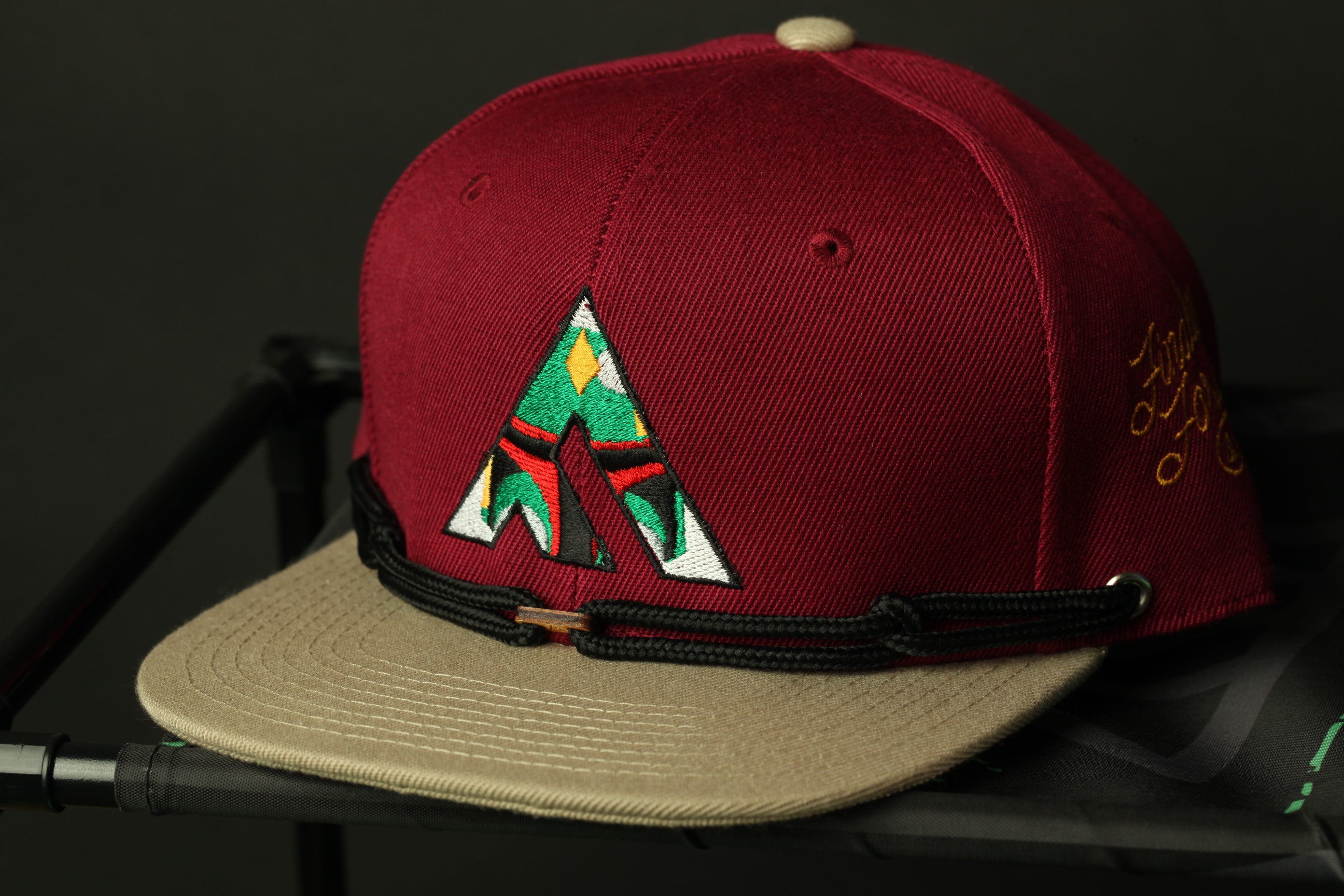 A maroon baseball cap with a colorful geometric pattern on the front, placed on a black surface.