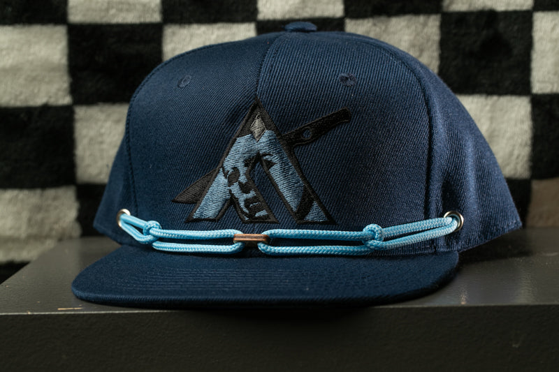A navy blue baseball cap with a black logo on the front, sitting on a black surface against a checkered background.