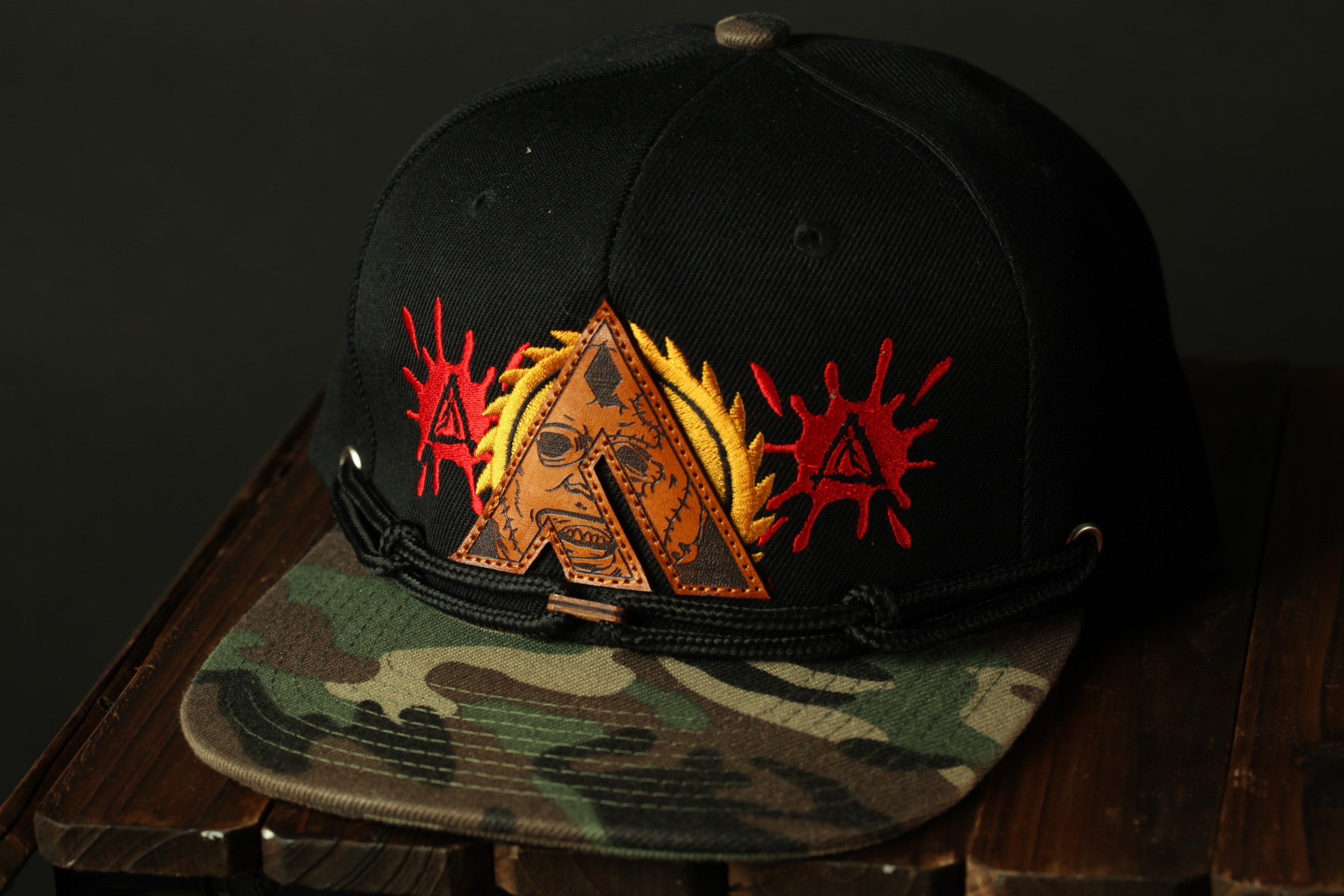 A black baseball cap with a camouflage pattern and a red and yellow design on the front.