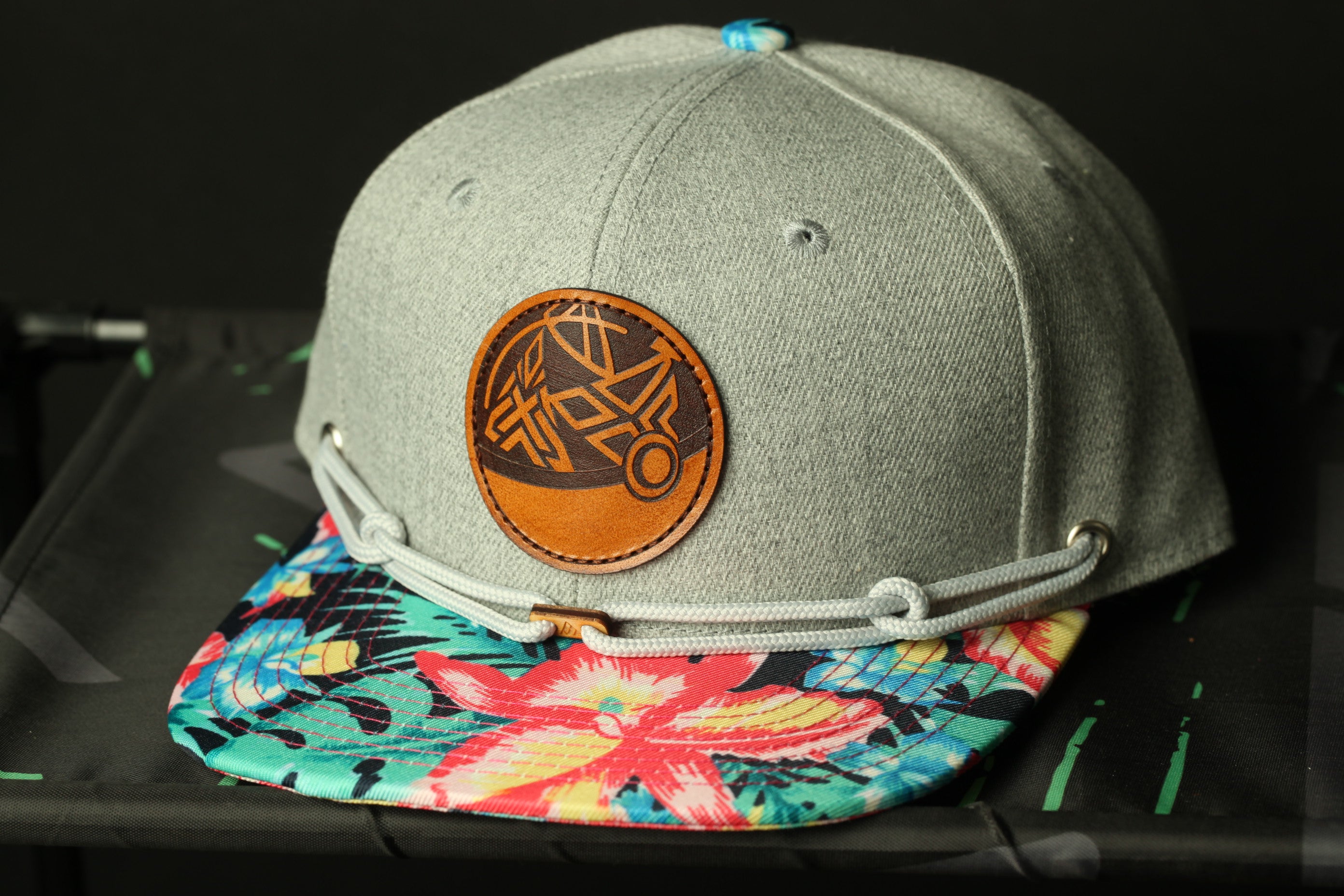 A gray baseball cap with a circular logo and a colorful floral pattern on the brim.
