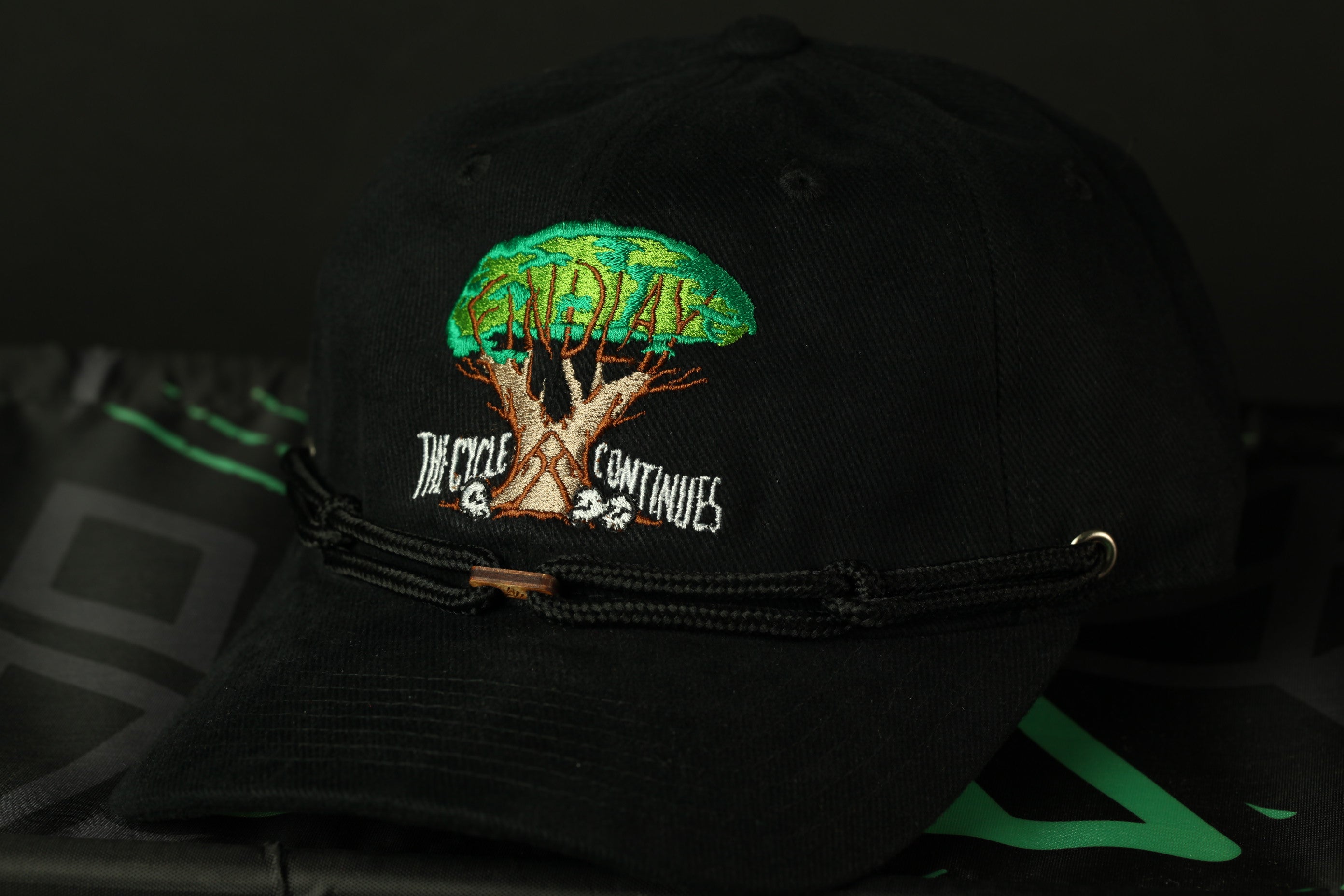 A black baseball cap with a tree design and text on it, resting on a black surface.