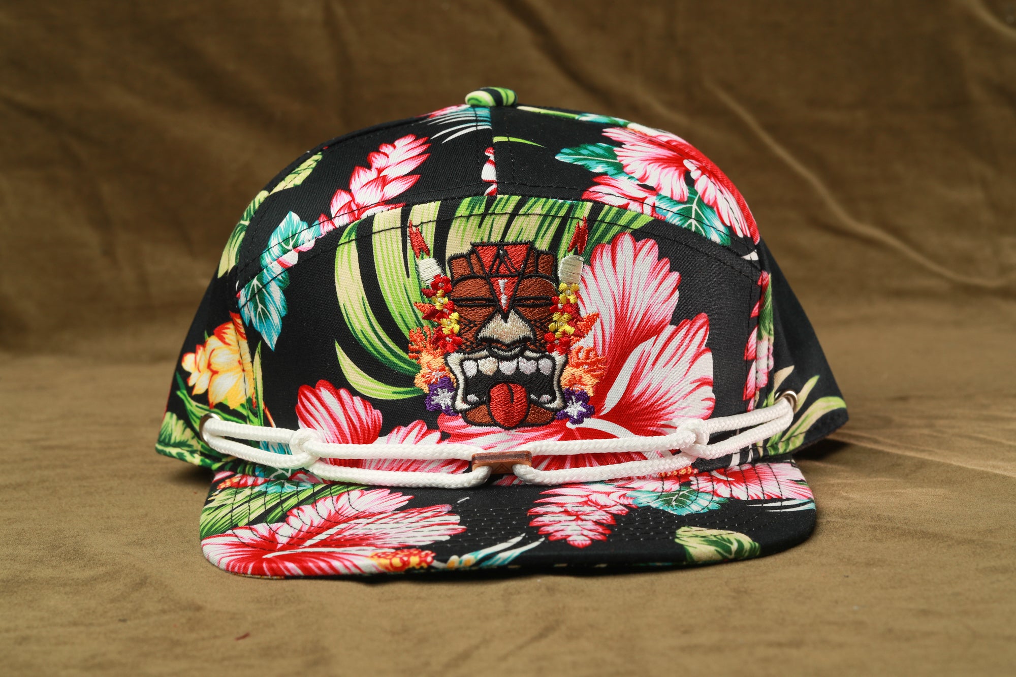 A colorful floral printed baseball cap with a tiki mask design on the front.