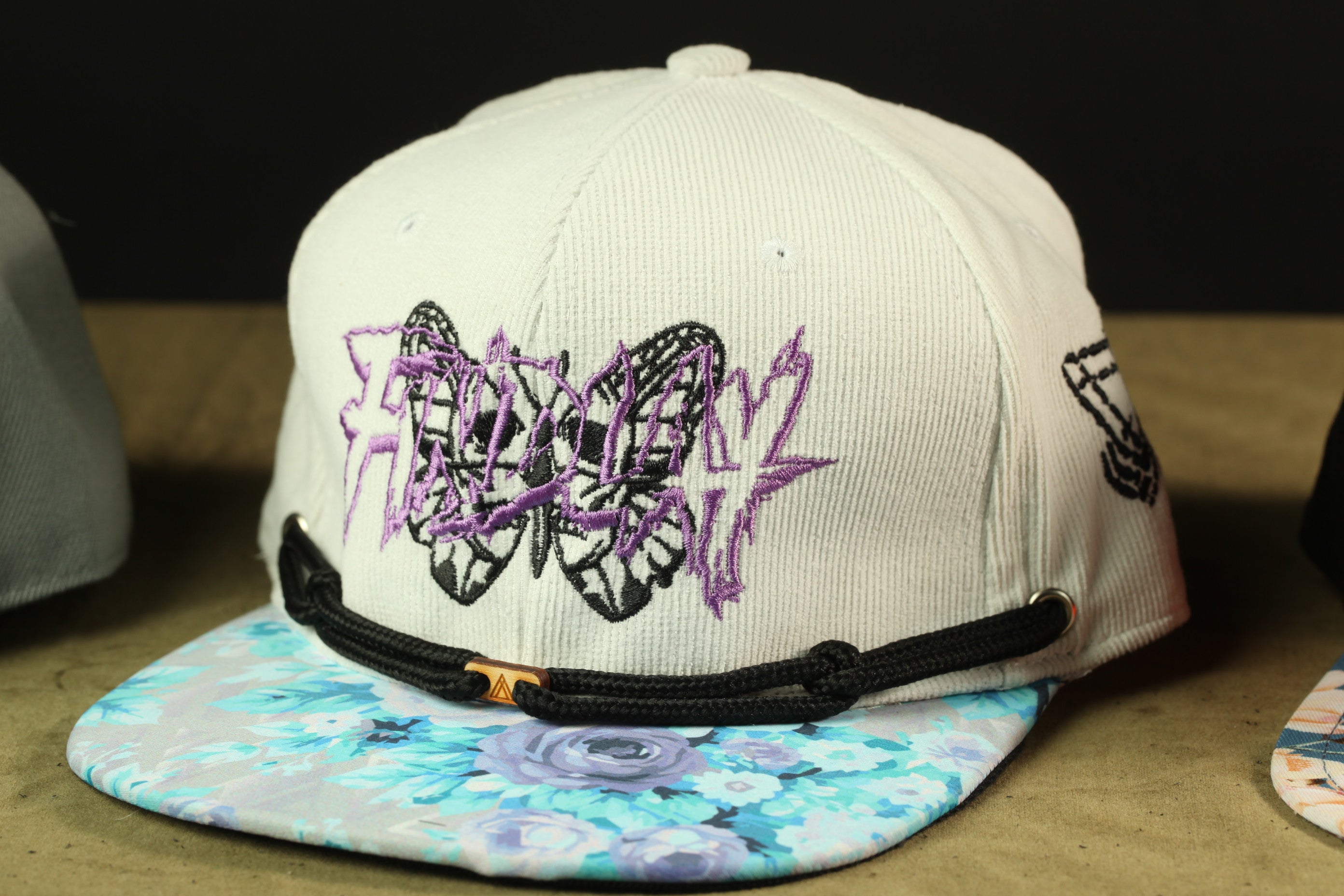 A white baseball cap with purple butterfly embroidery and a floral pattern on the brim.