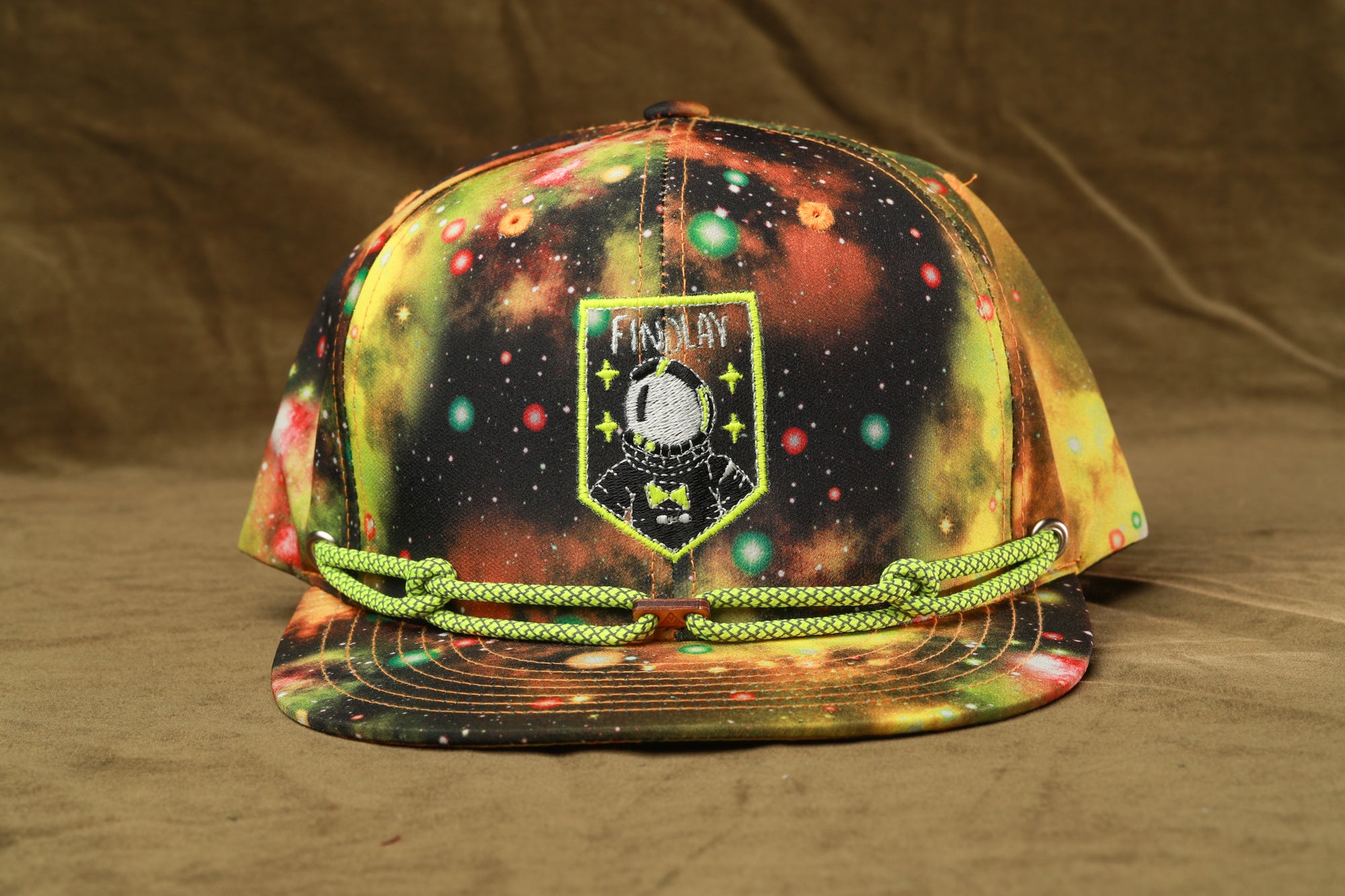 A colorful, patterned baseball cap with a space-themed design, featuring a patch with a space illustration and the word "FINDlay" printed on it.