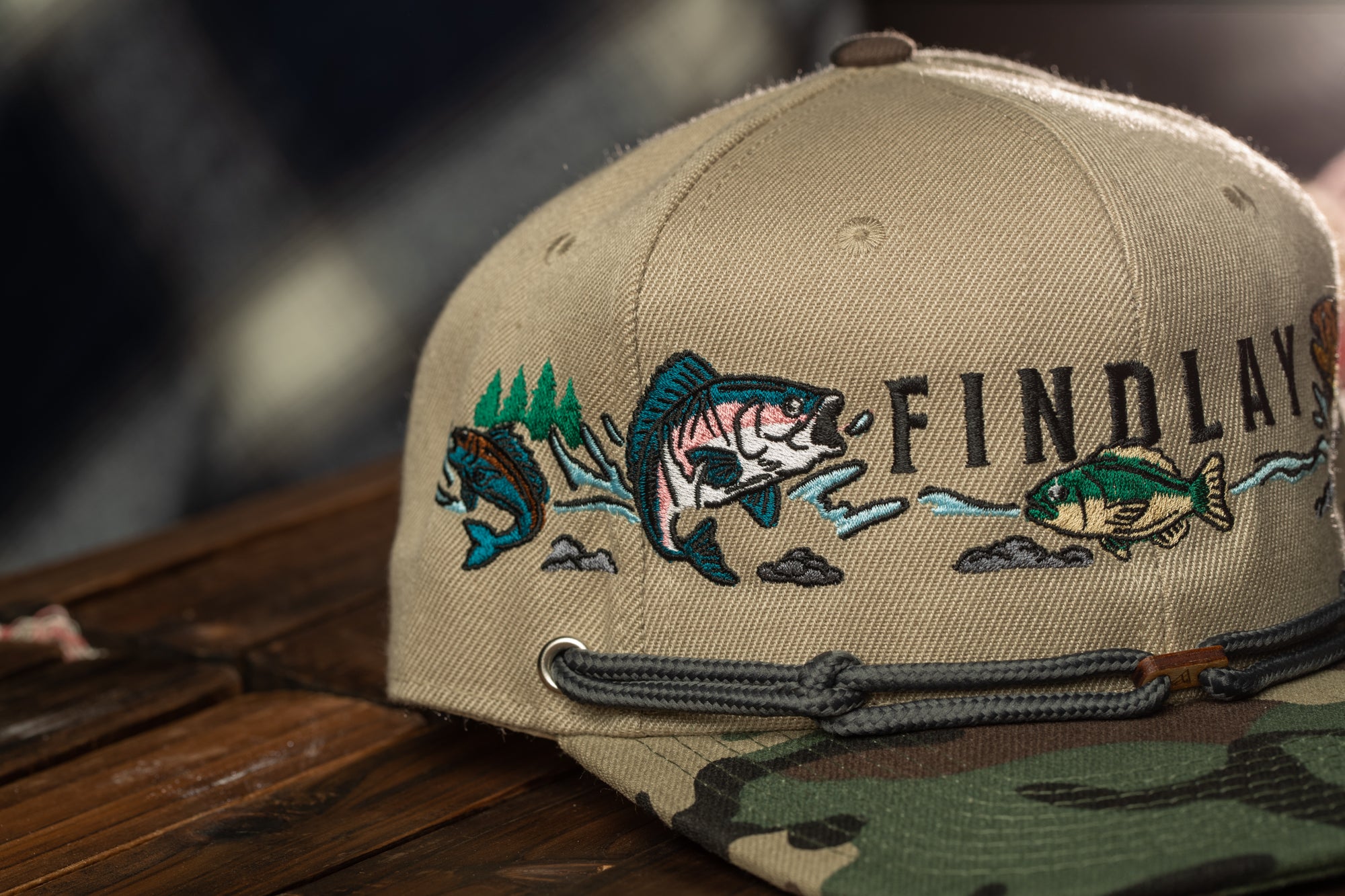 A tan baseball cap with embroidered fish designs on the front, sitting on a wooden surface.