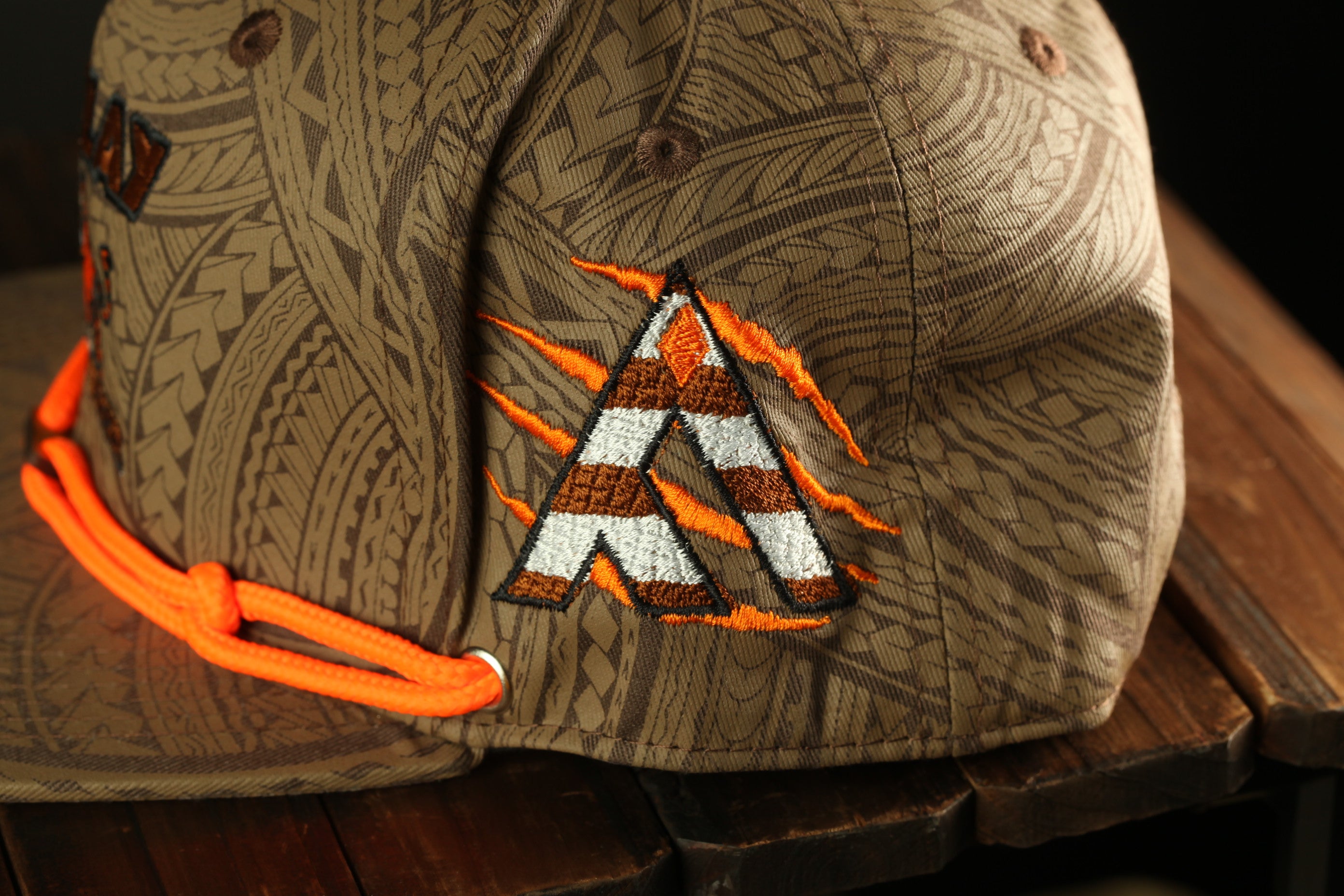 A close-up view of a brown baseball cap with a distinctive orange and white logo on the side.