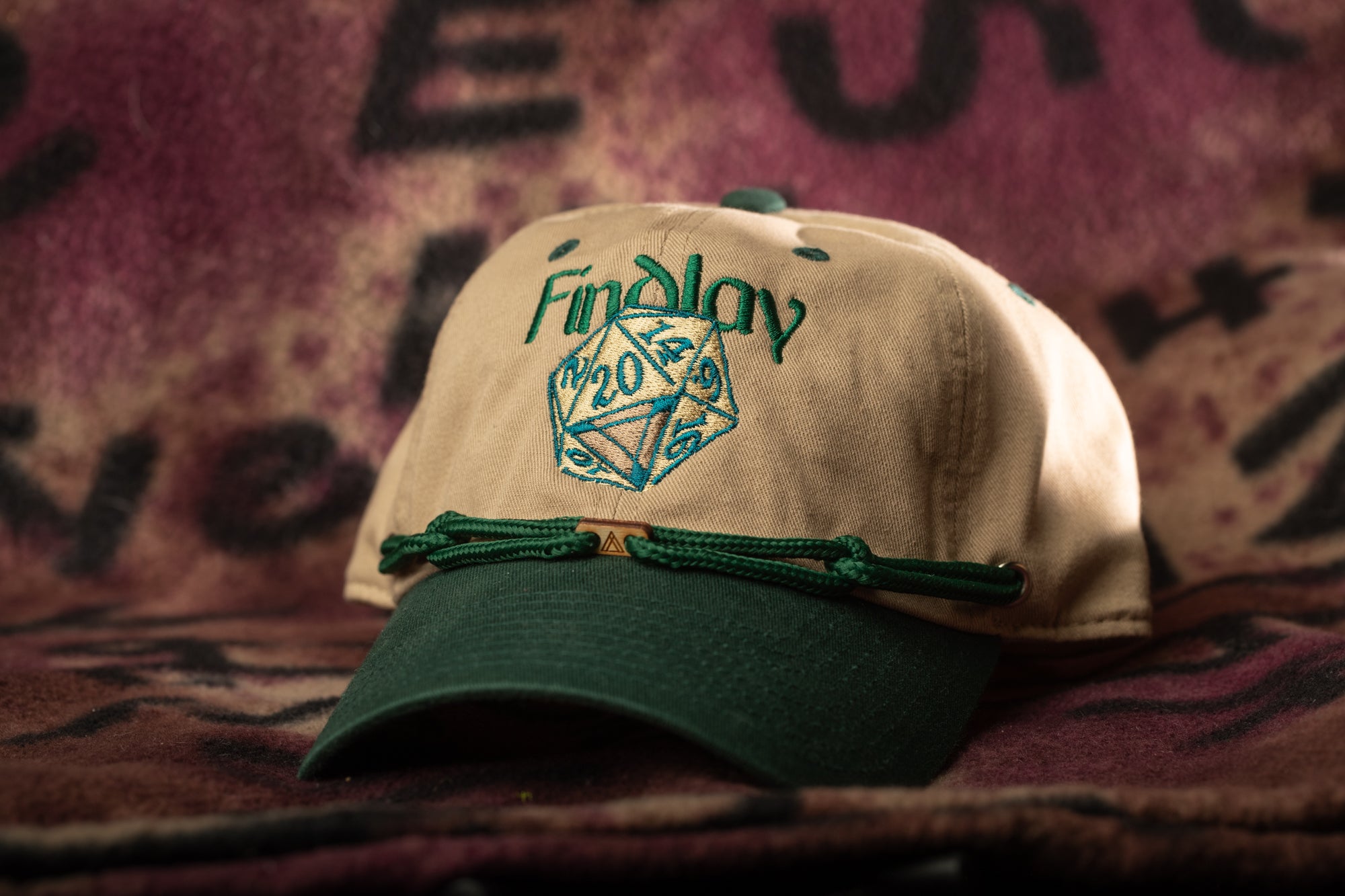 A beige baseball cap with a green brim and a green string, featuring a logo with the text "Findlay" on it.