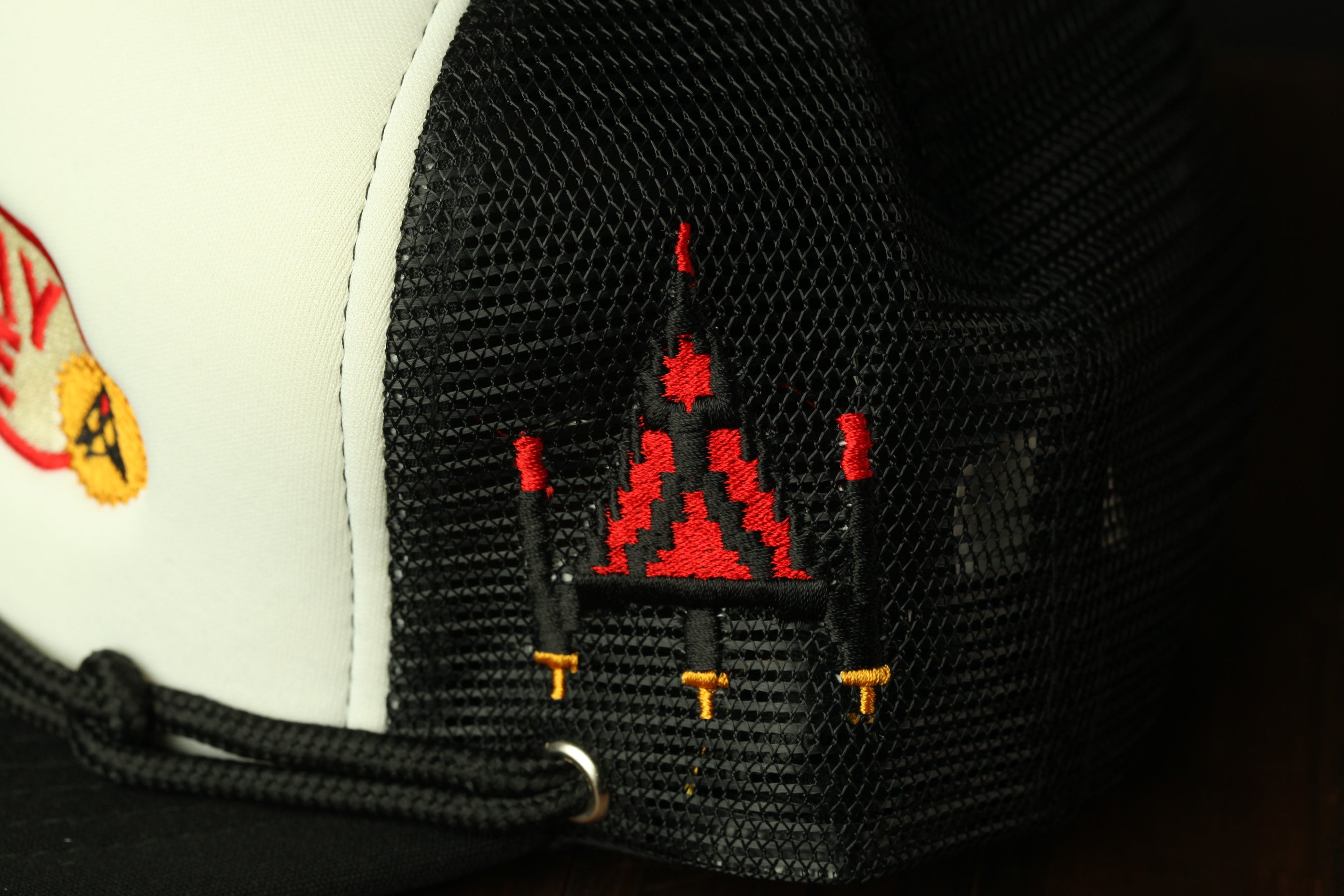 a close-up view of a black and white baseball cap with a red and black embroidered design on the side.