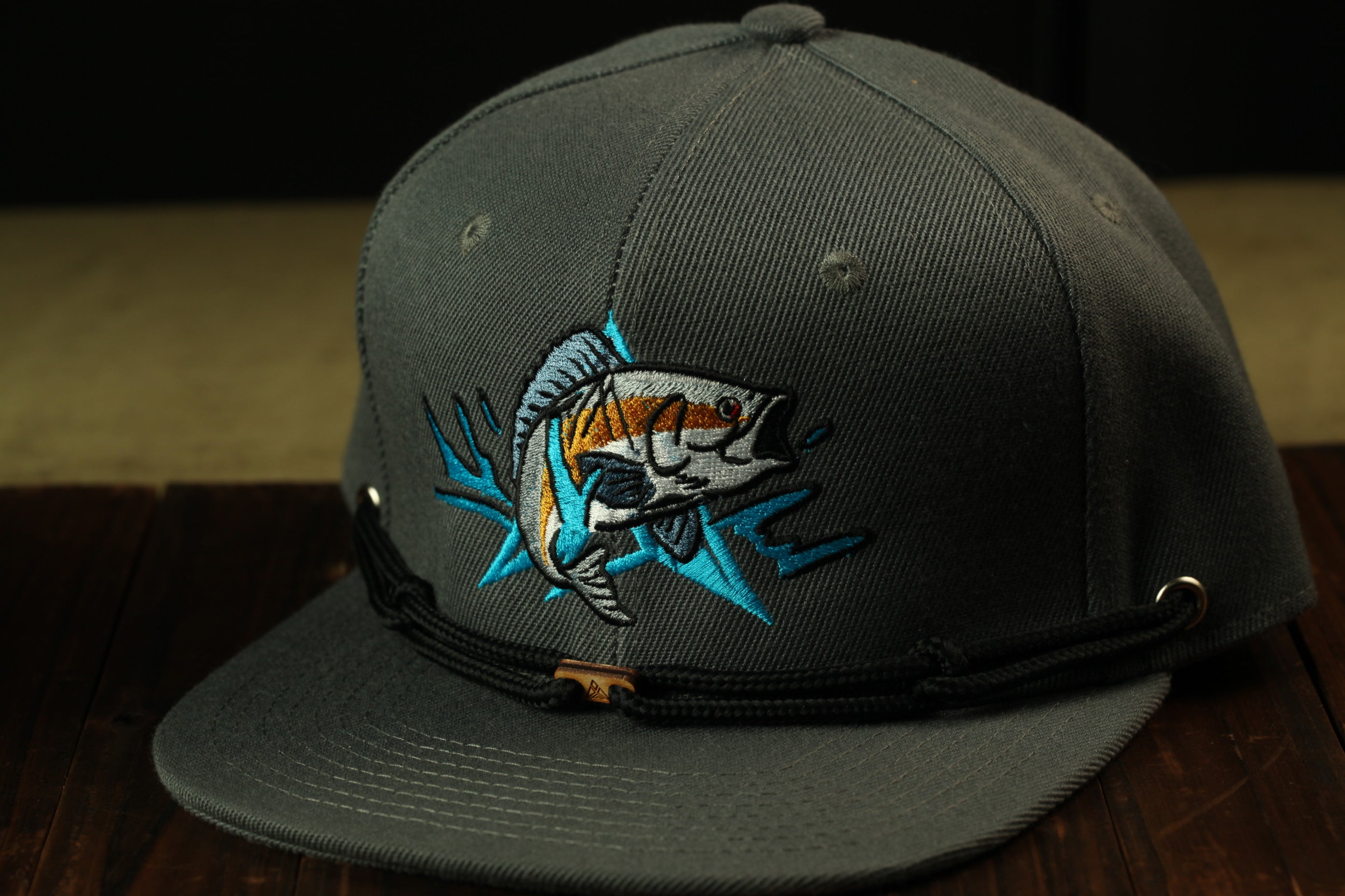 A gray baseball cap with a fish embroidered on it, sitting on a wooden surface.