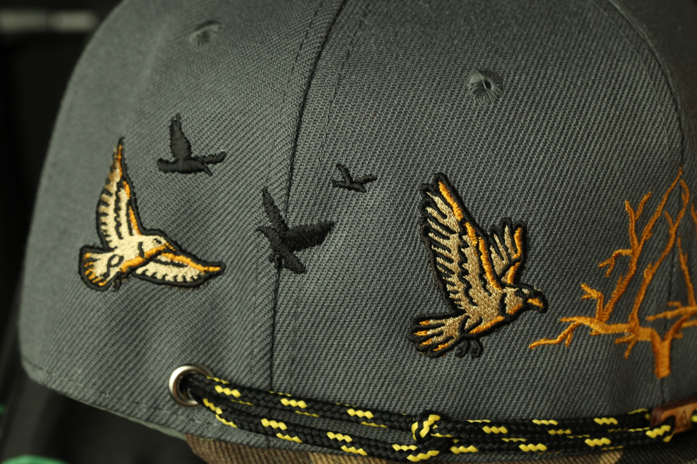 a close-up view of a gray baseball cap with various bird embroidered designs on it.