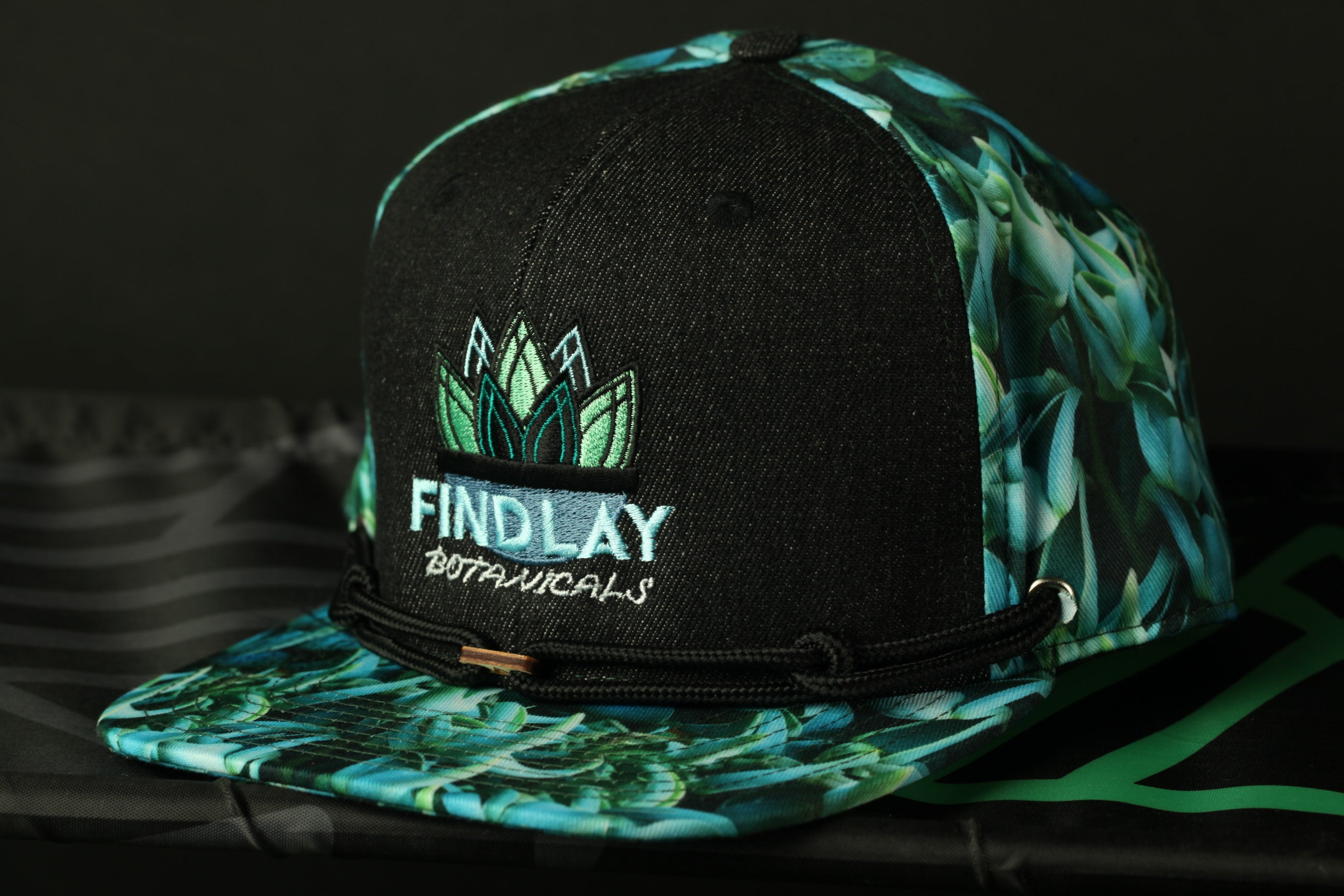 A black baseball cap with a floral print pattern and the text "FINDLAY BOTANICALS" printed on it.