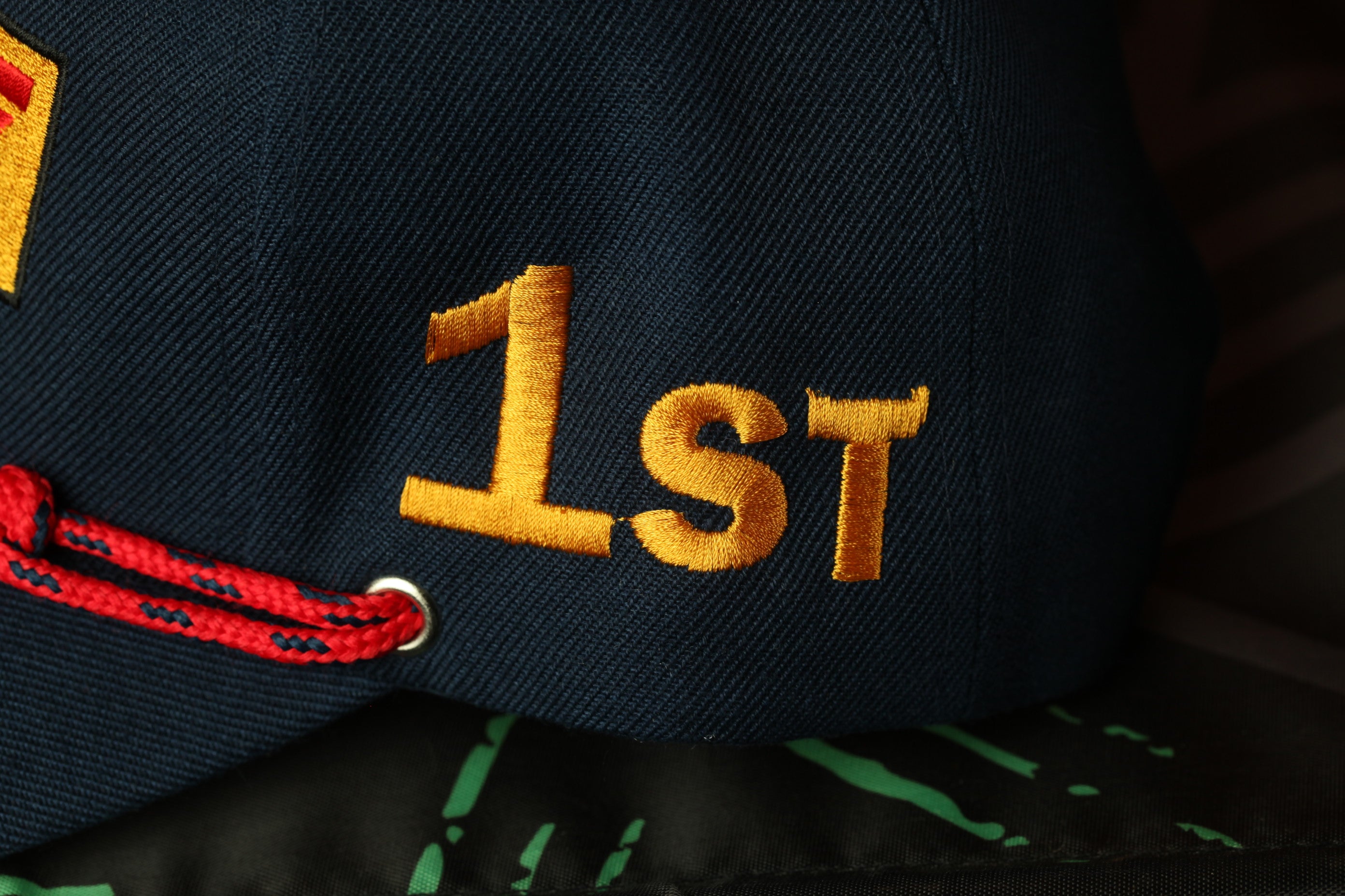 A close-up view of a dark blue baseball cap with the number "1st" embroidered on it in gold.