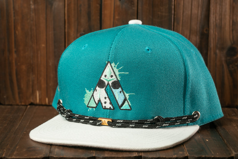 A turquoise baseball cap with a white brim and a black and white patterned strap is displayed on a wooden surface.