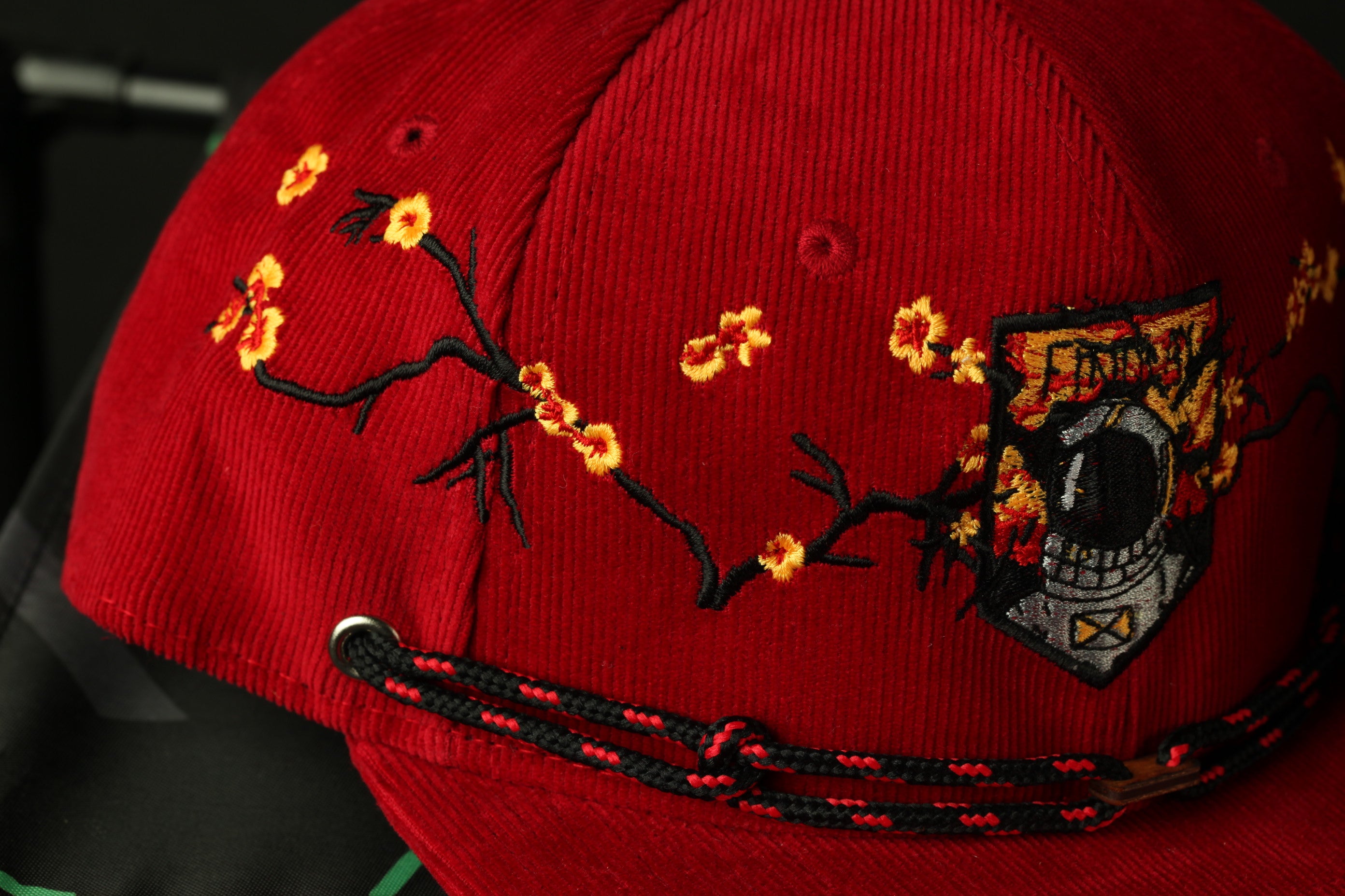 A close-up view of a red baseball cap with a floral design and a patch on the front.