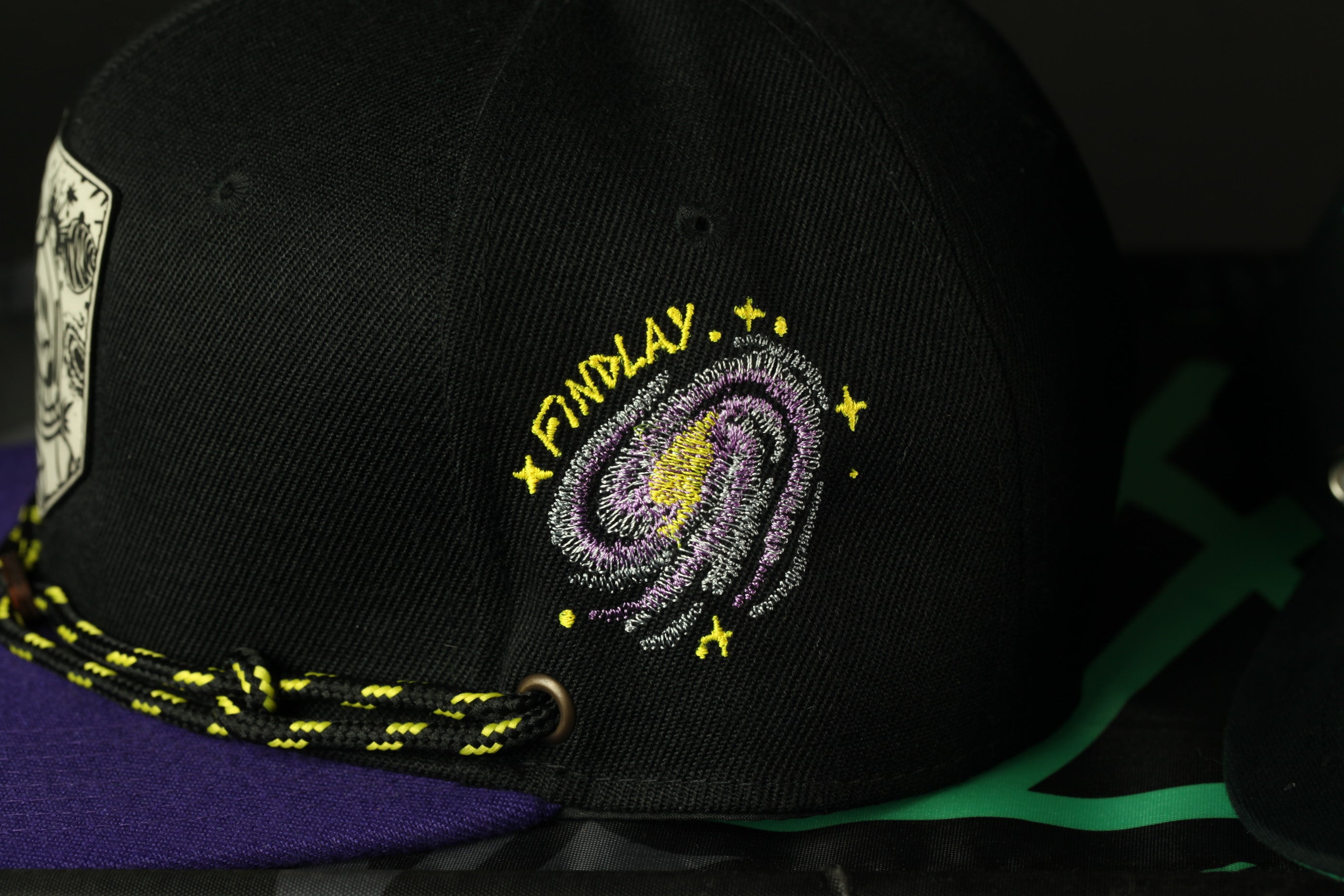 A black baseball cap with a colorful embroidered design on the front, featuring a galaxy-like pattern and the word "FINDlay" written on it.